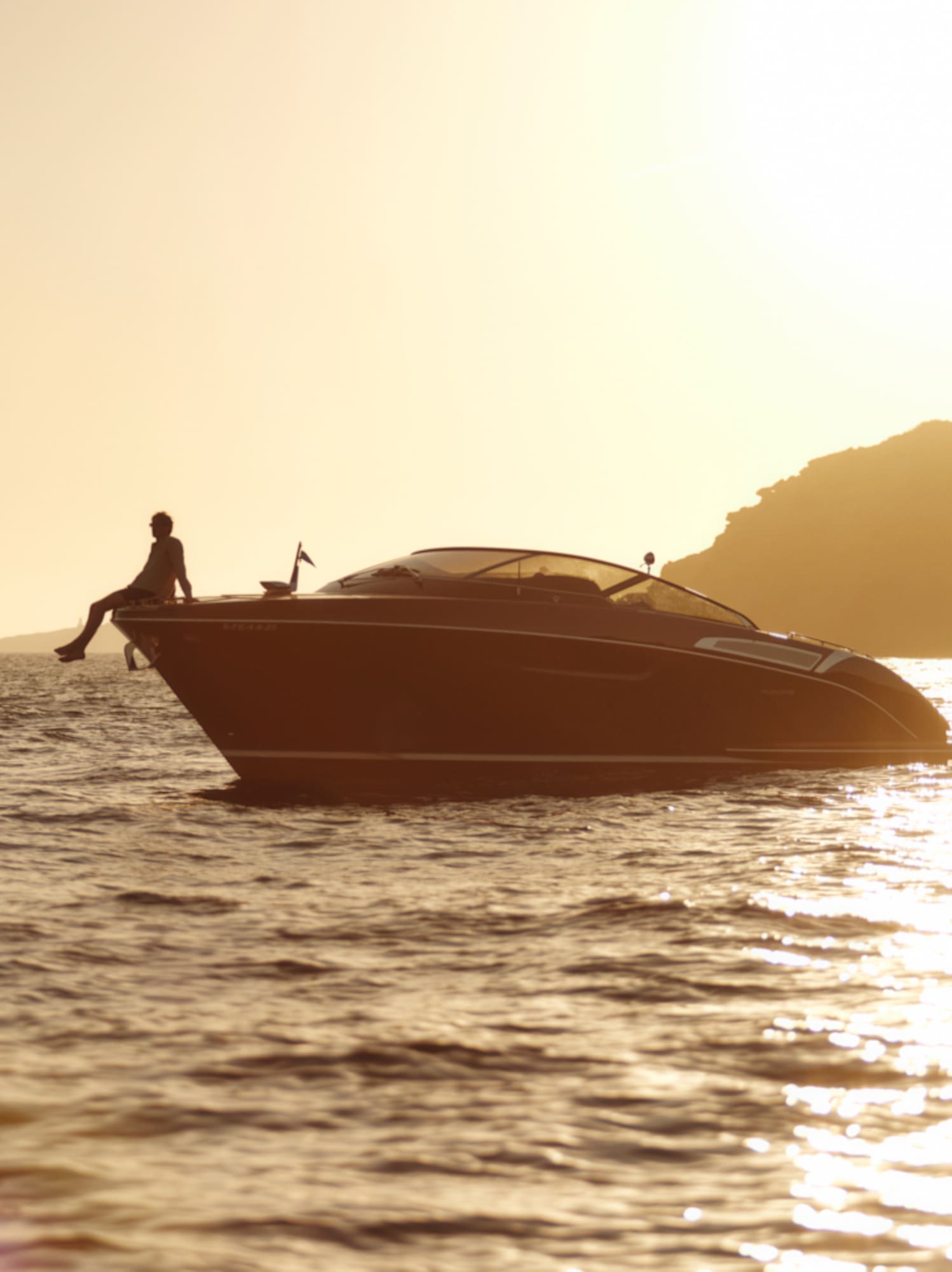 Person on luxury yacht, silhouetted at golden sunset over sparkling water.