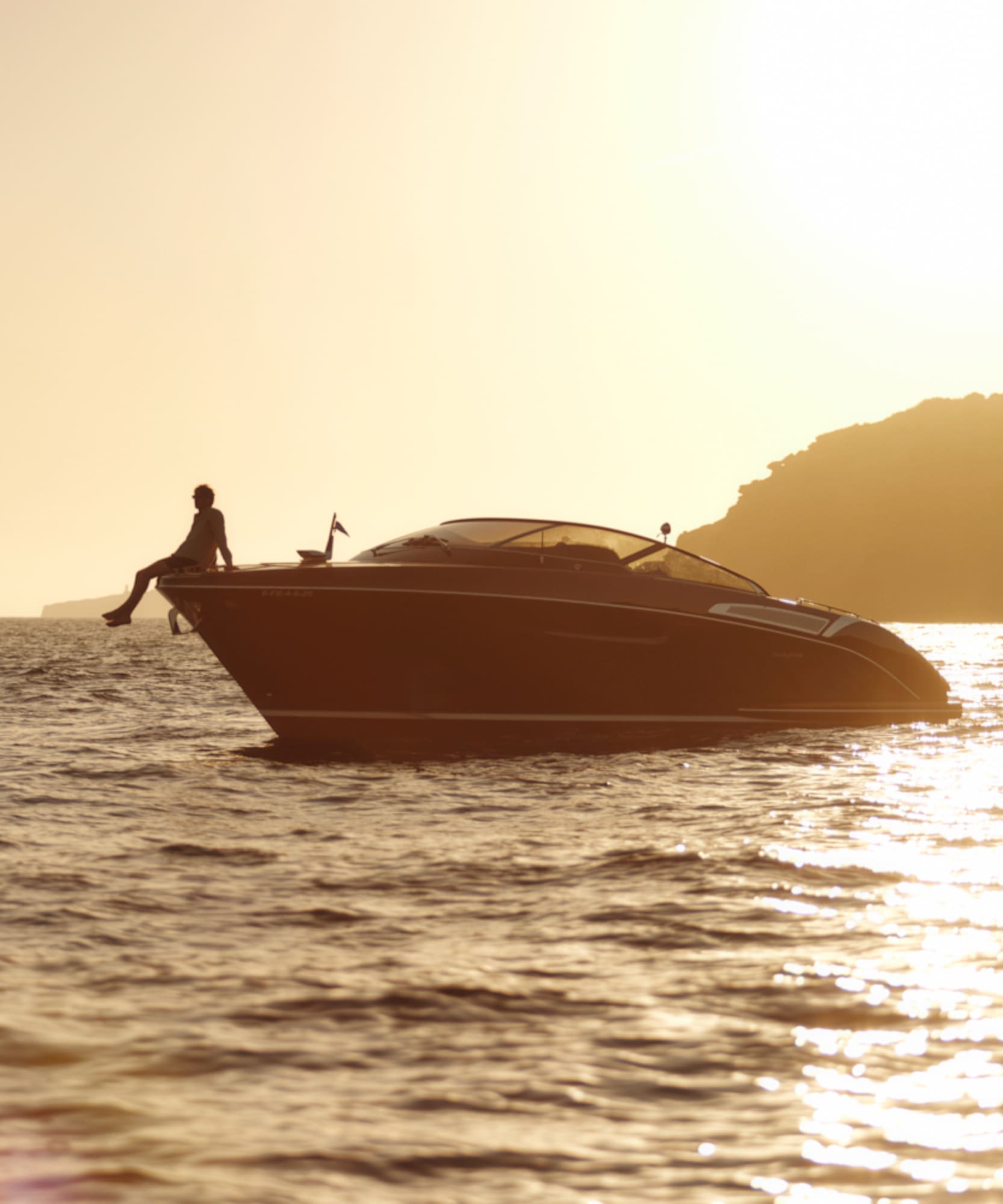 Silhouette of person on luxury boat at golden sunset, sparkling ocean.