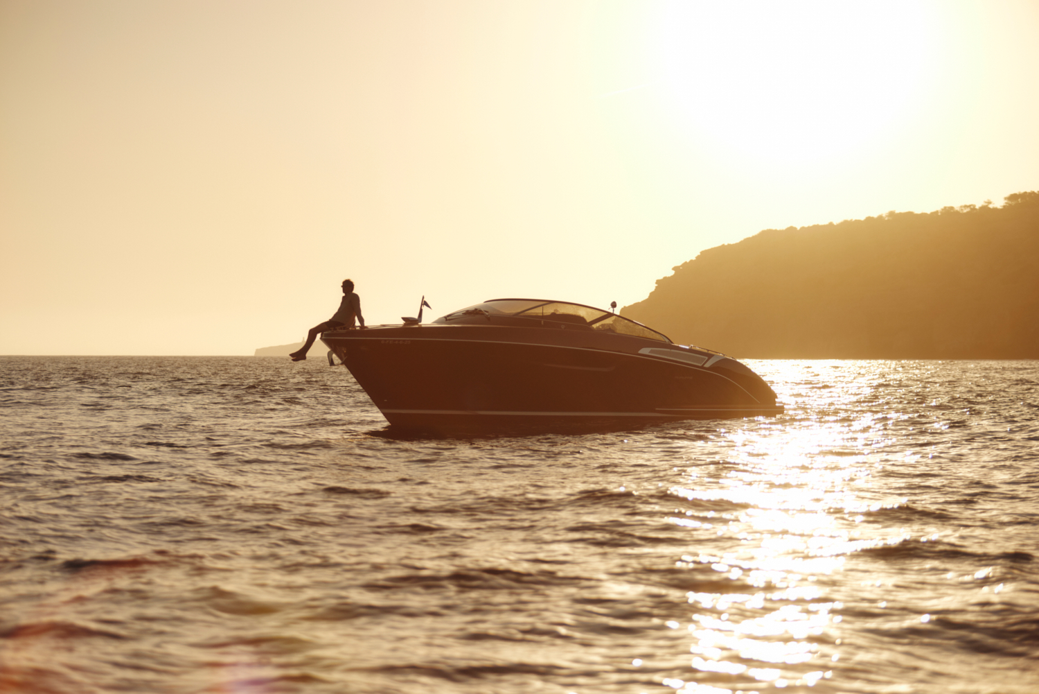 Person on luxury yacht, silhouetted at golden sunset over sparkling water.