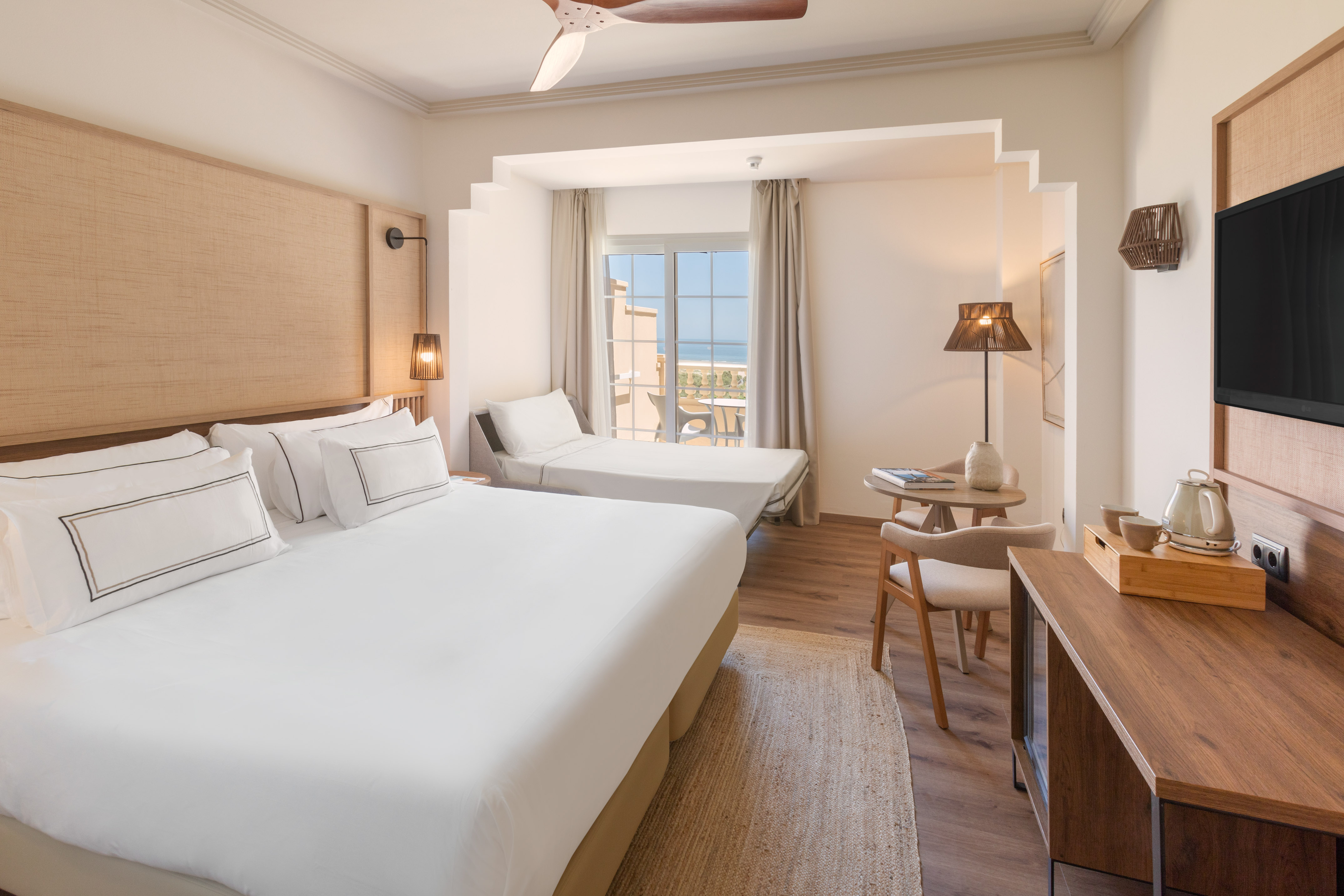 Spacious modern hotel room with double bed, sofa bed, and a sea view balcony.