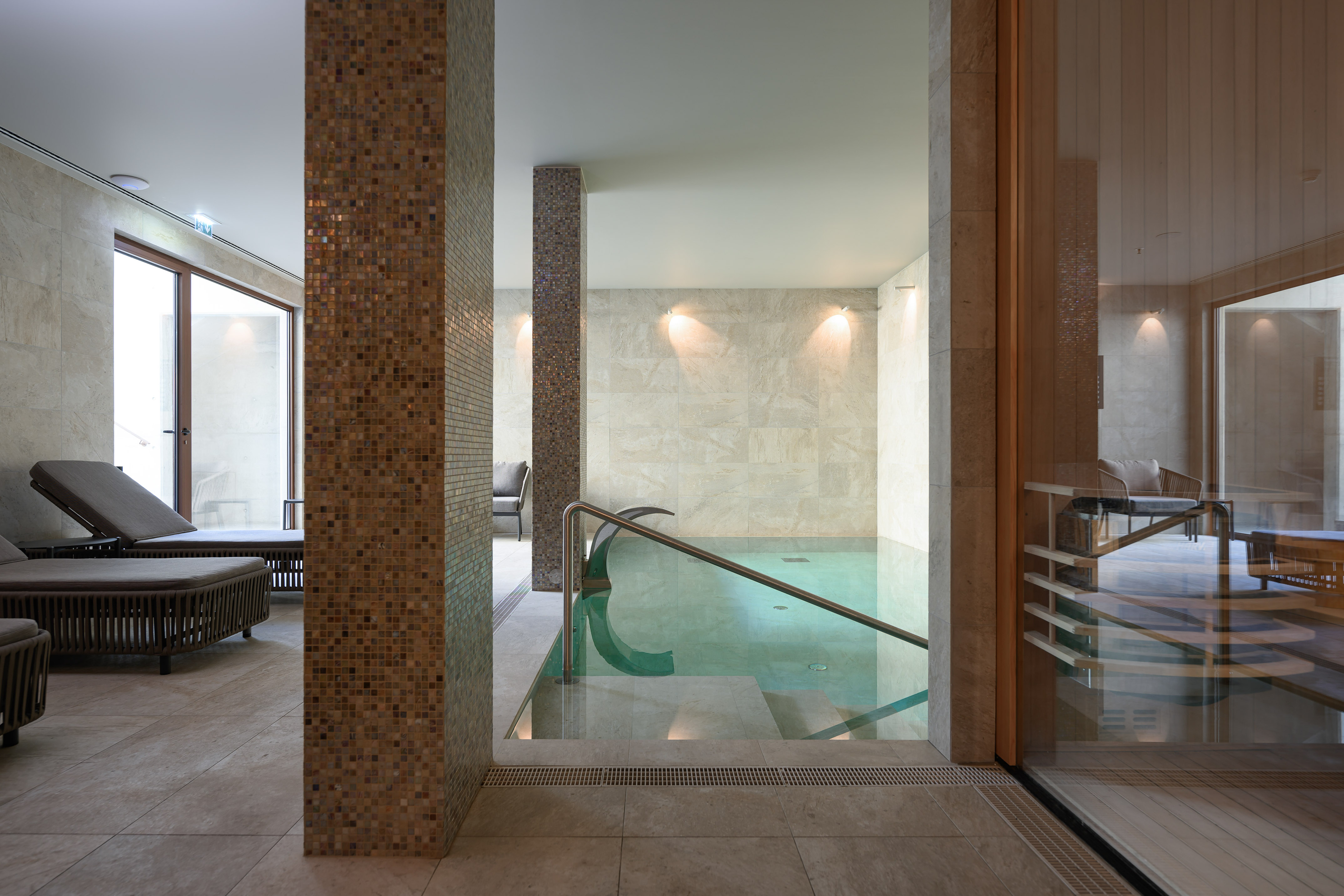 Indoor spa pool with modern design, mosaic columns, and lounge beds.