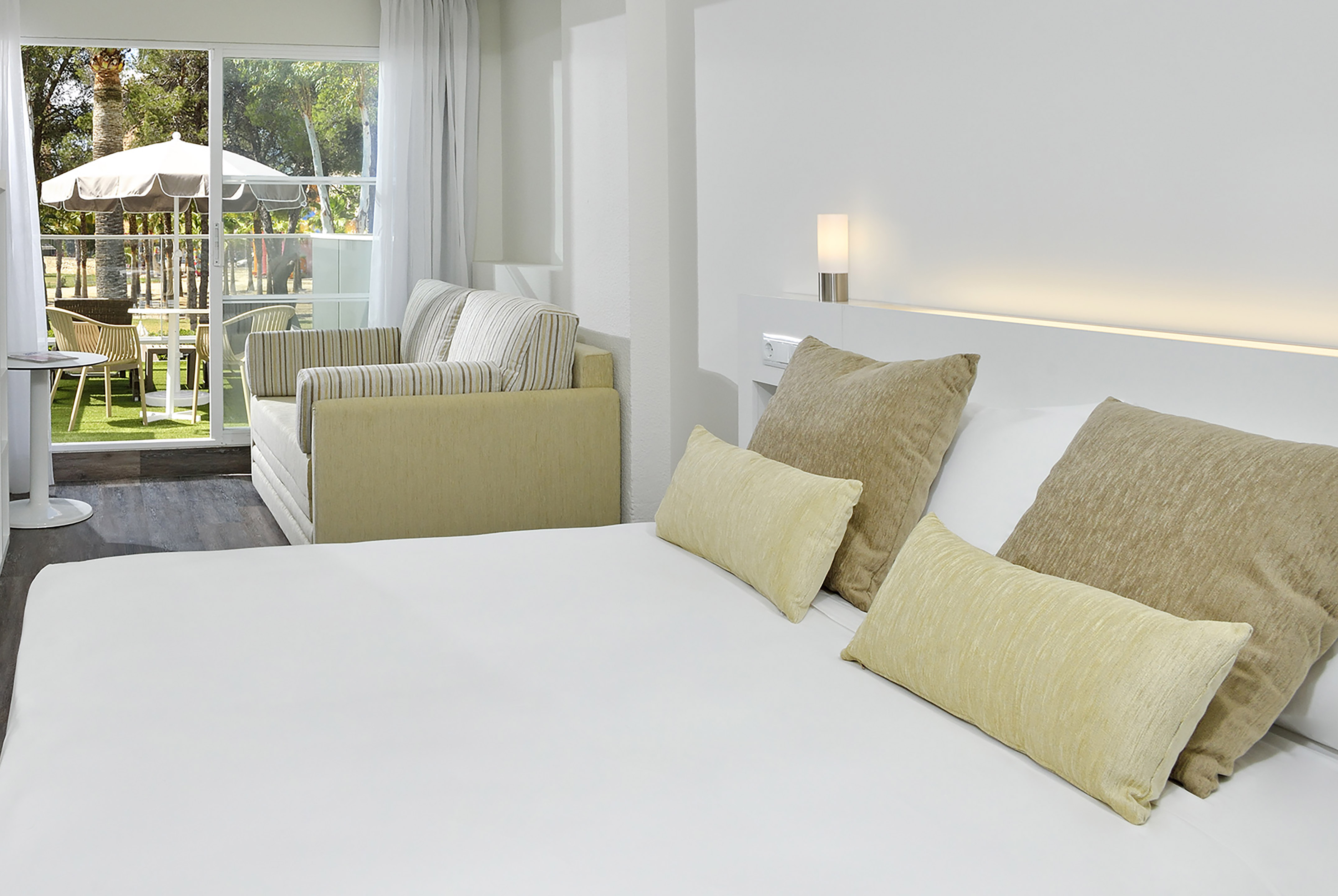 Modern hotel room with bed, sofa, and patio doors to garden view.