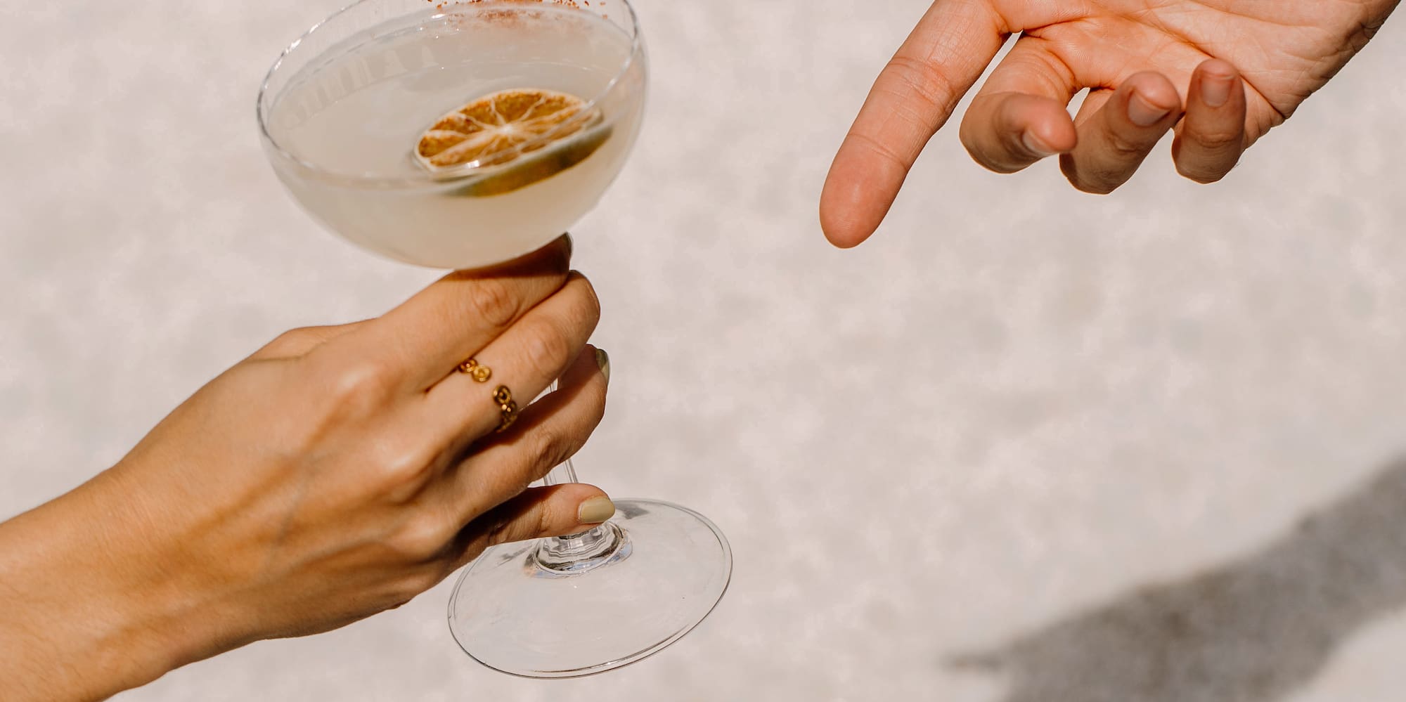 Mano ofreciendo cóctel con lima y borde de chile, otra mano alcanzando.