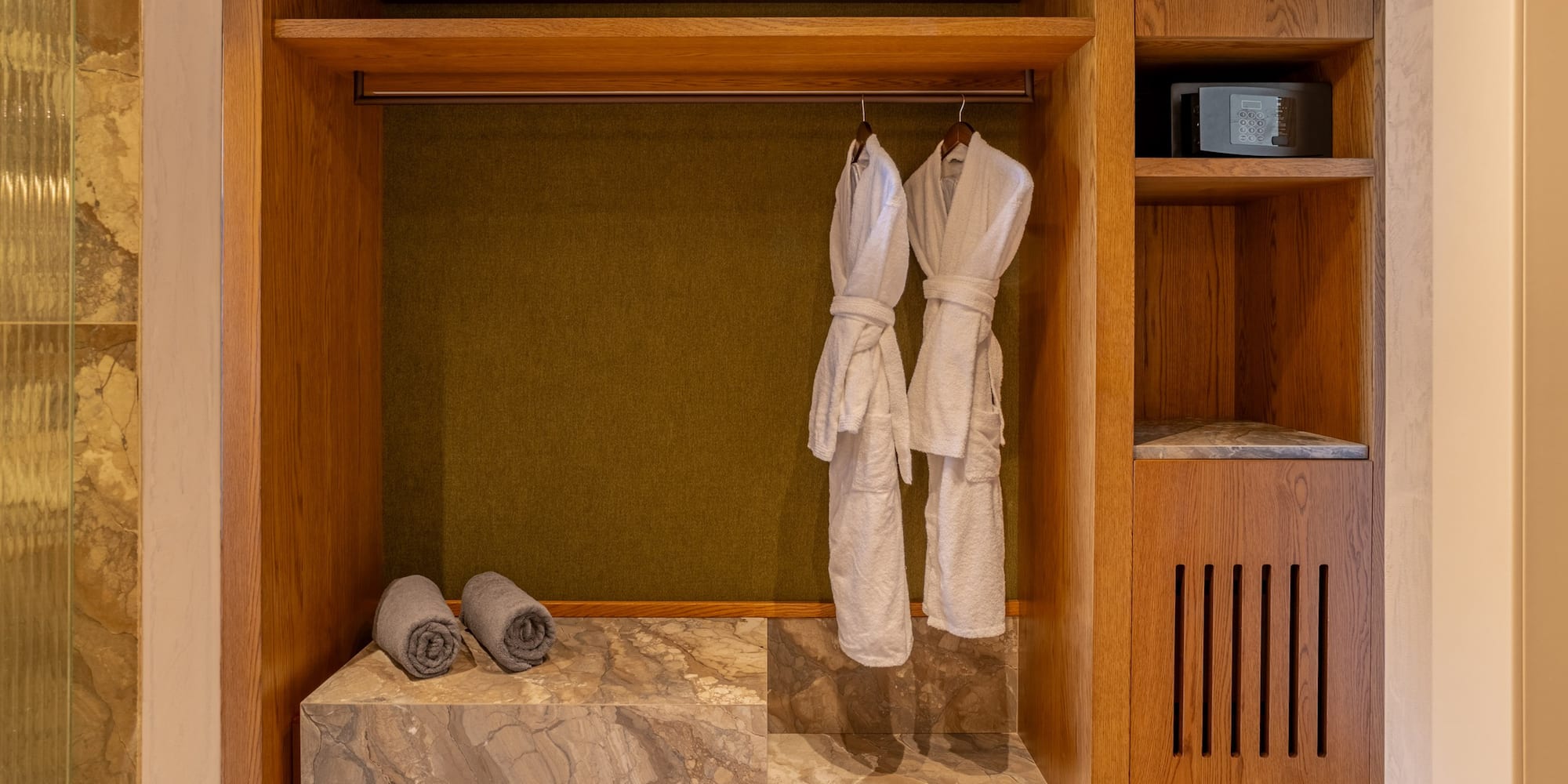 Wooden hotel closet with white bathrobes, grey towels, and security safe.