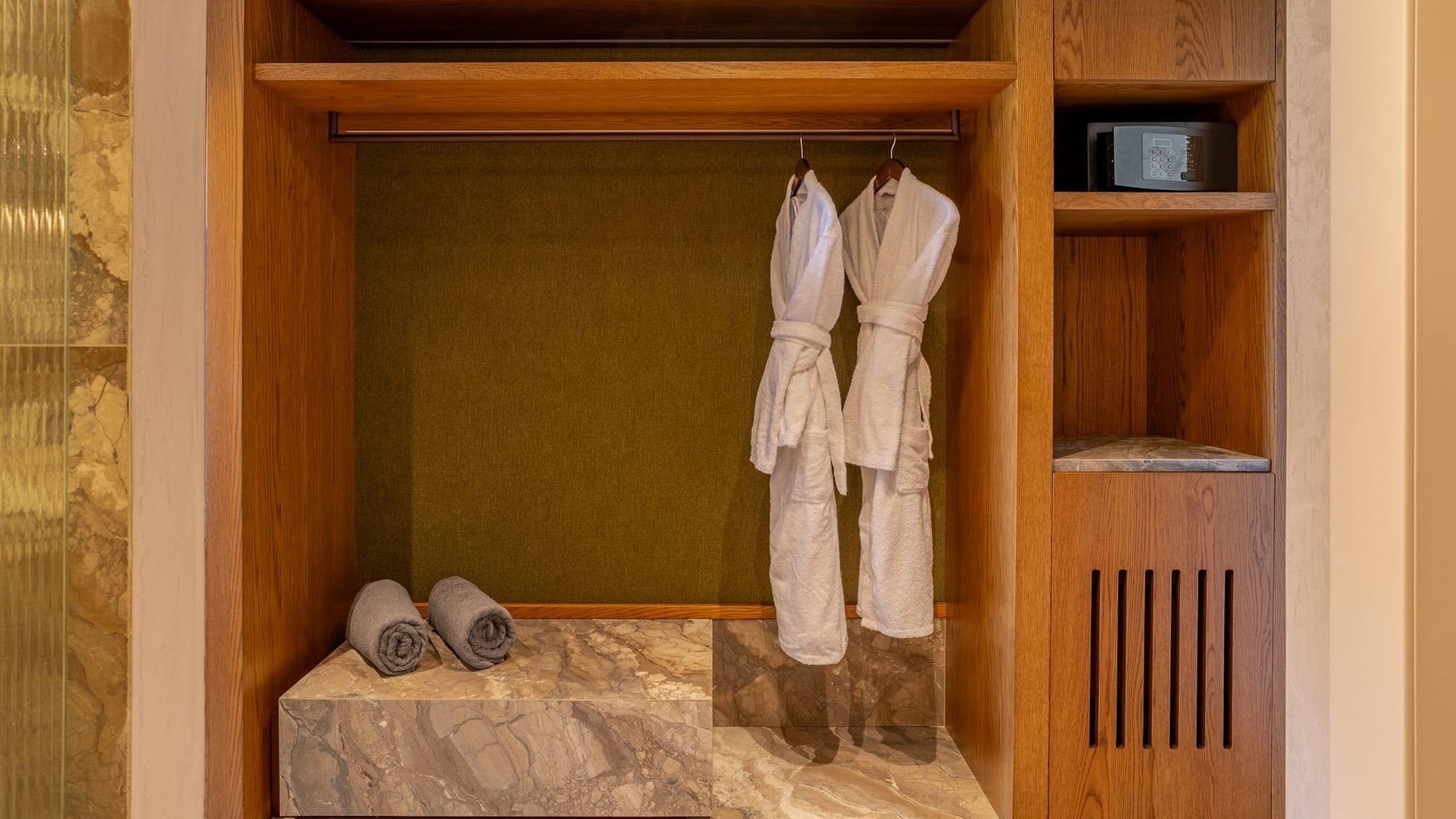 Wooden hotel closet with white bathrobes, grey towels, and security safe.