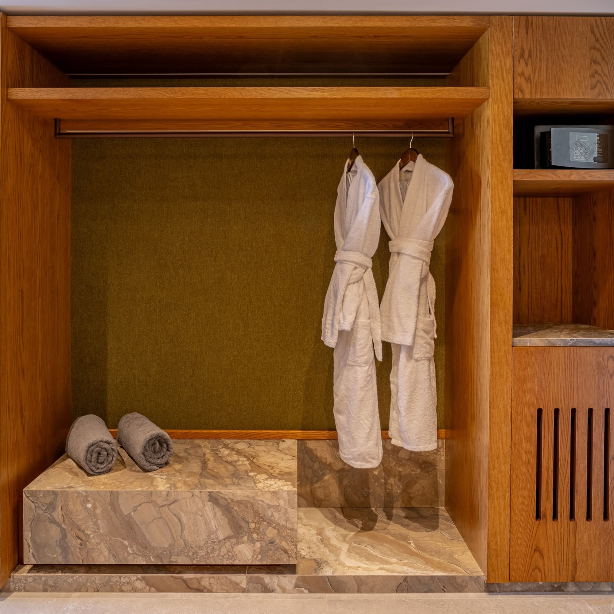 Wooden hotel closet with white bathrobes, grey towels, and security safe.