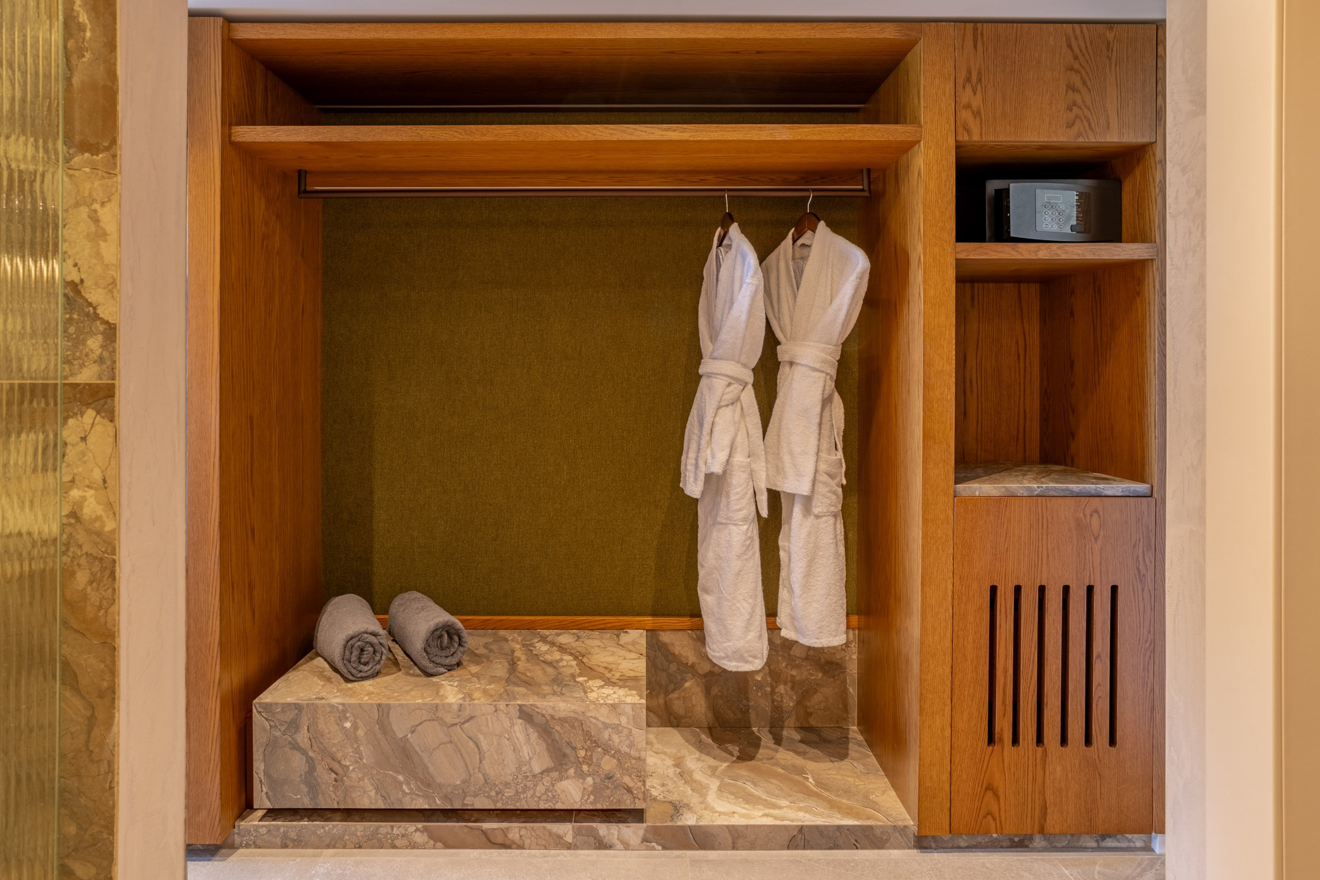 Wooden hotel closet with white bathrobes, grey towels, and security safe.