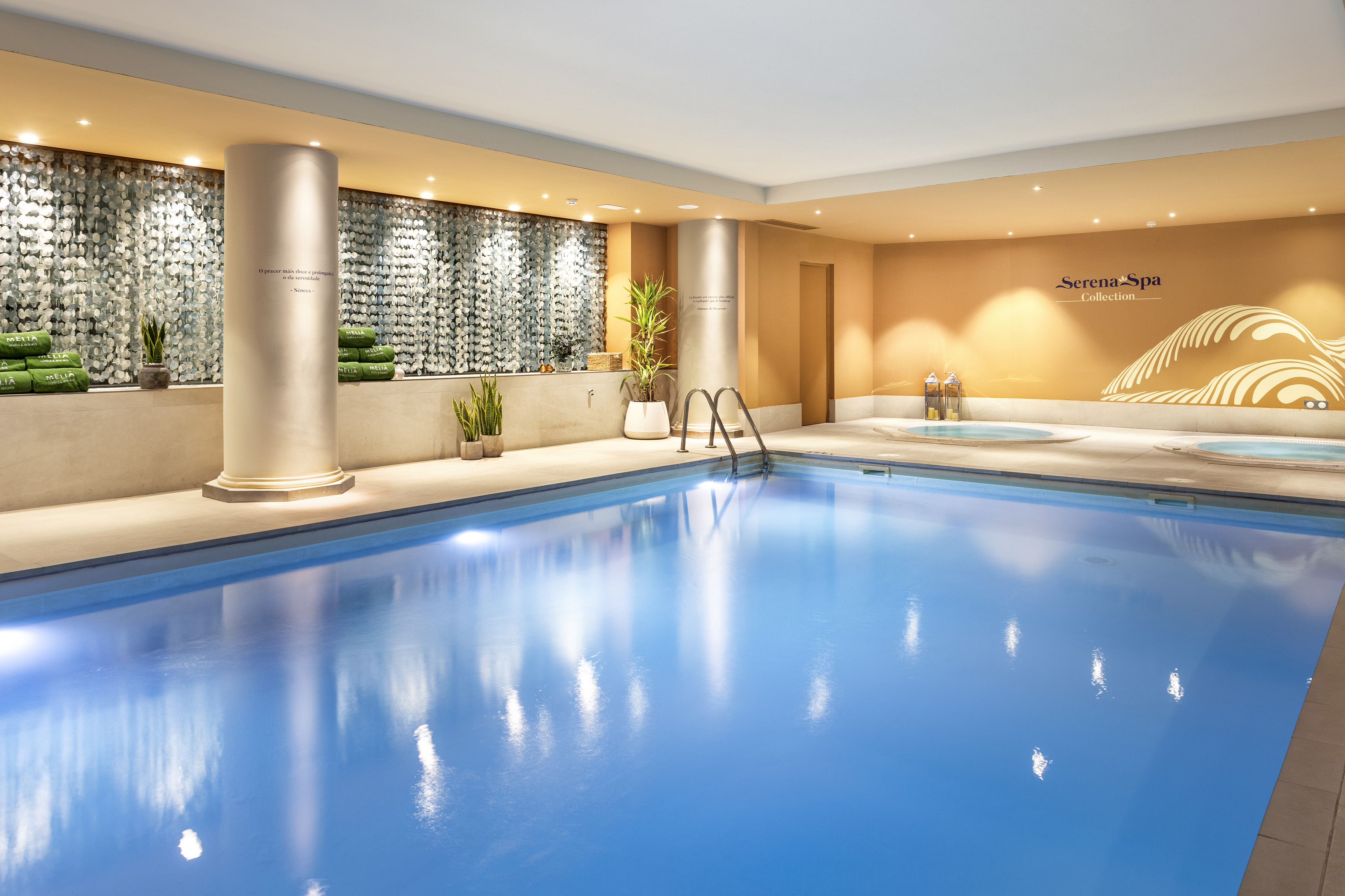 Luxurious indoor spa pool with two jacuzzis and soft lighting.