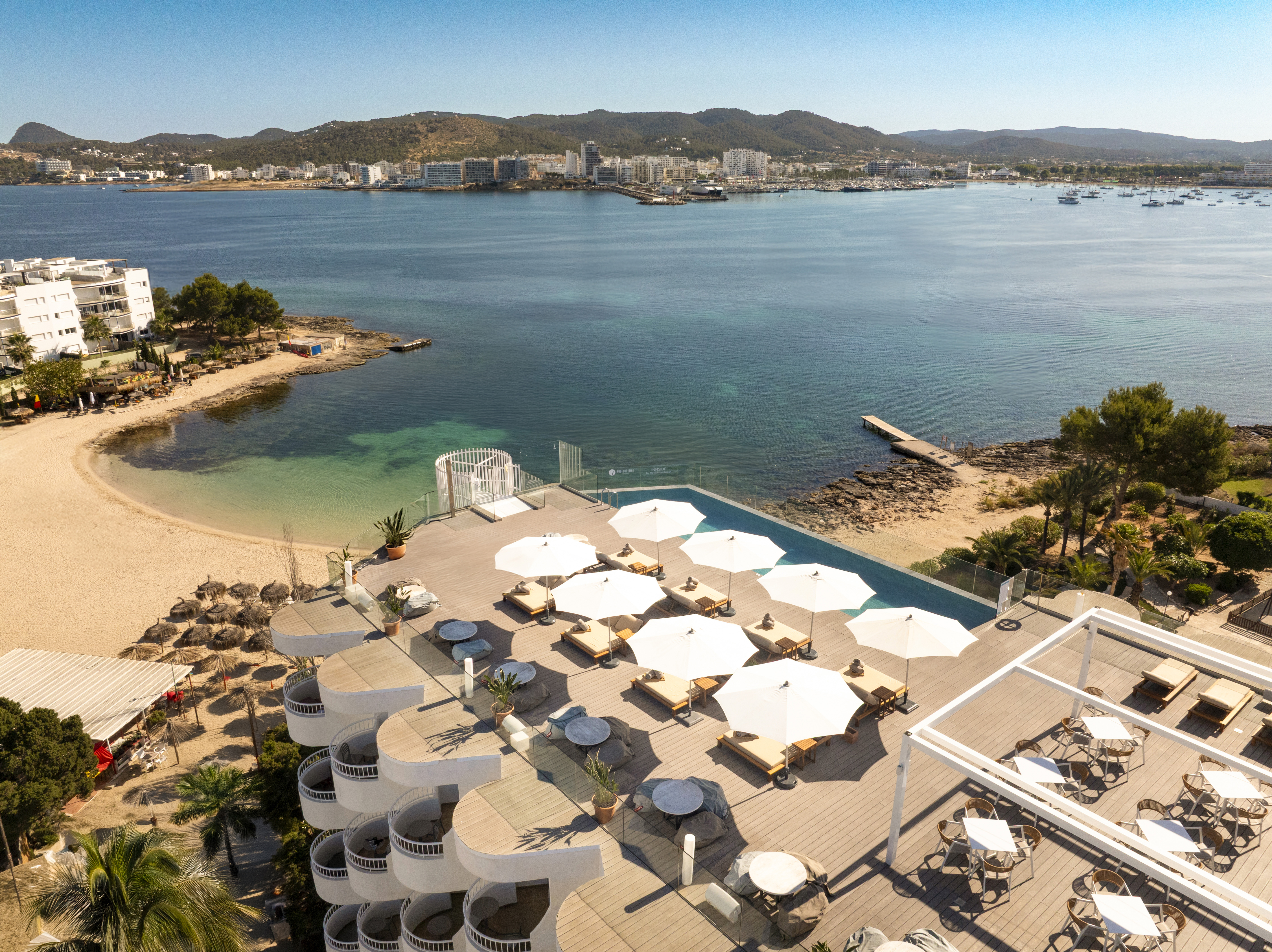 Luxury Ibiza resort: rooftop infinity pool, beach, clear blue bay.