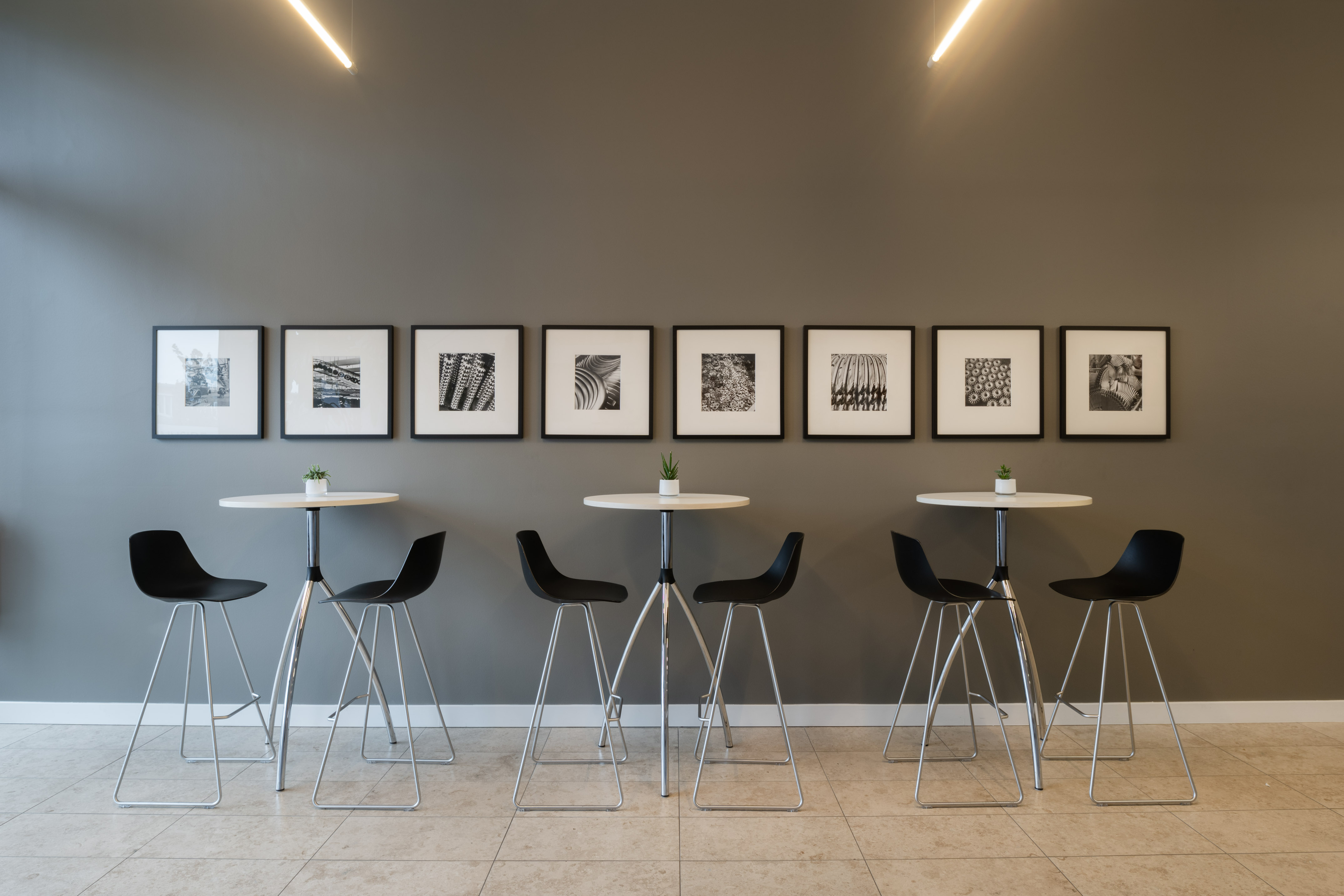 Modern office high-top tables with black stools and framed wall art.