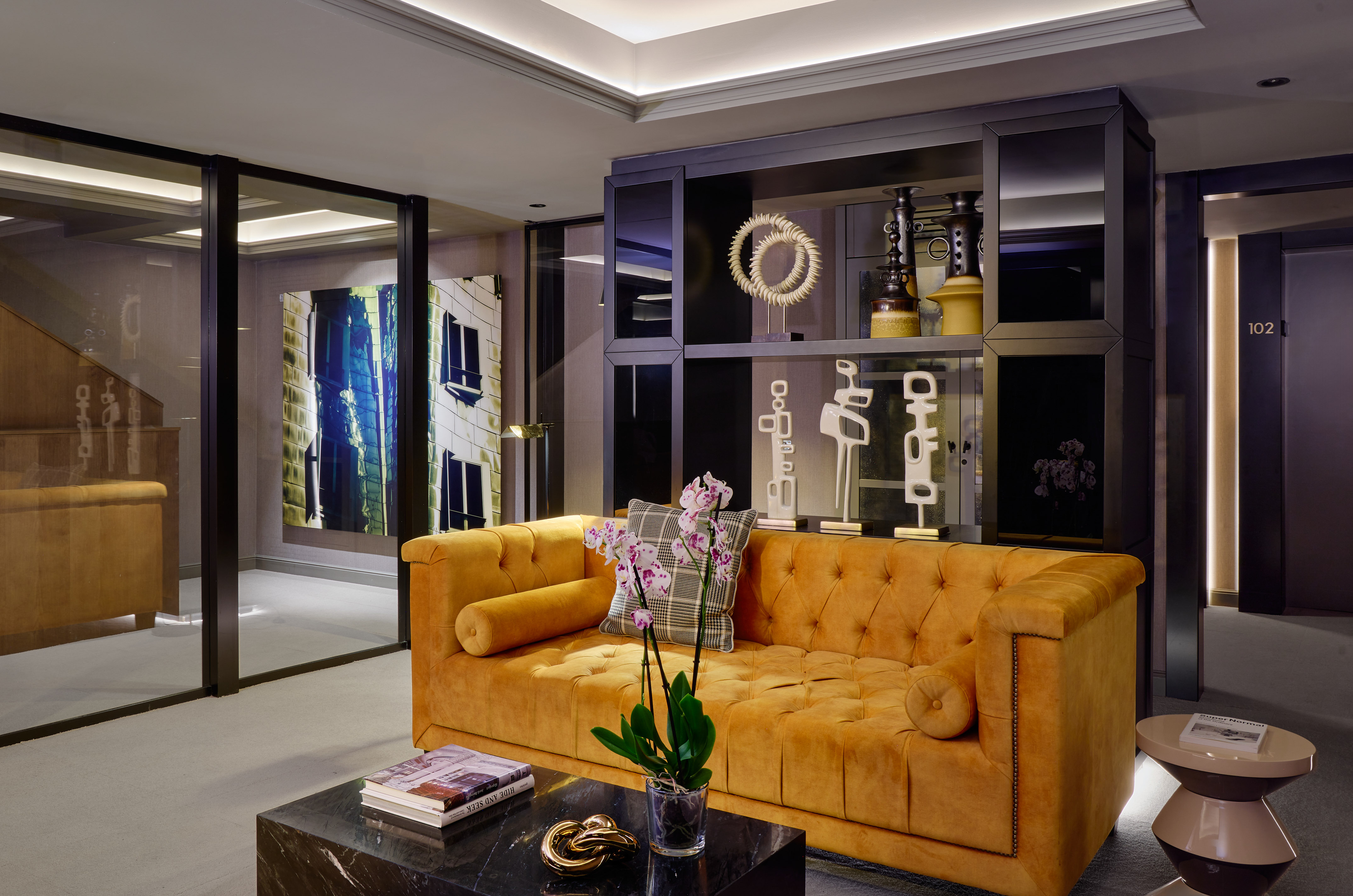 Modern hotel lounge with orange tufted sofa, black marble table, abstract art.