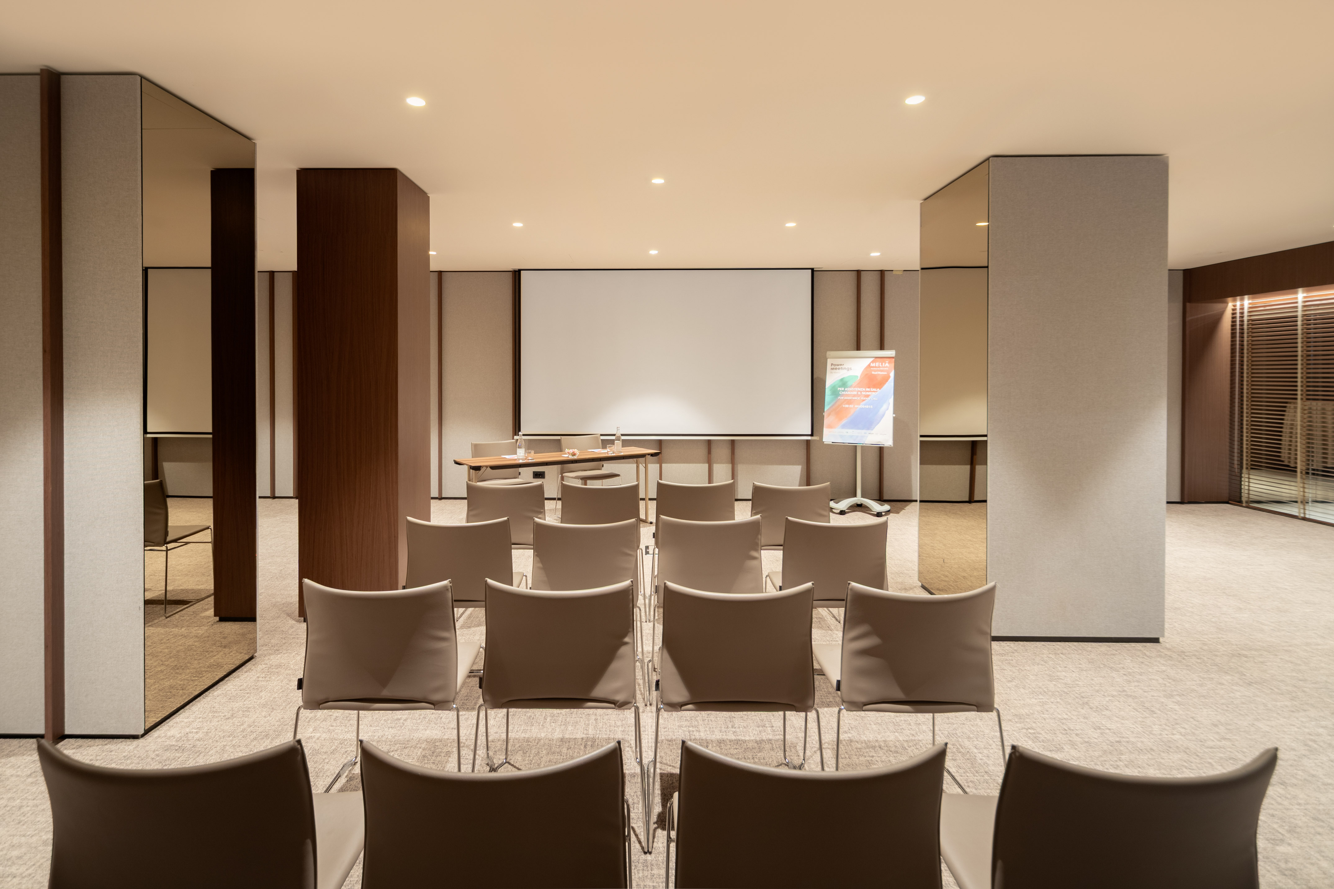 Modern meeting room with beige chairs, projector screen, and flip chart.