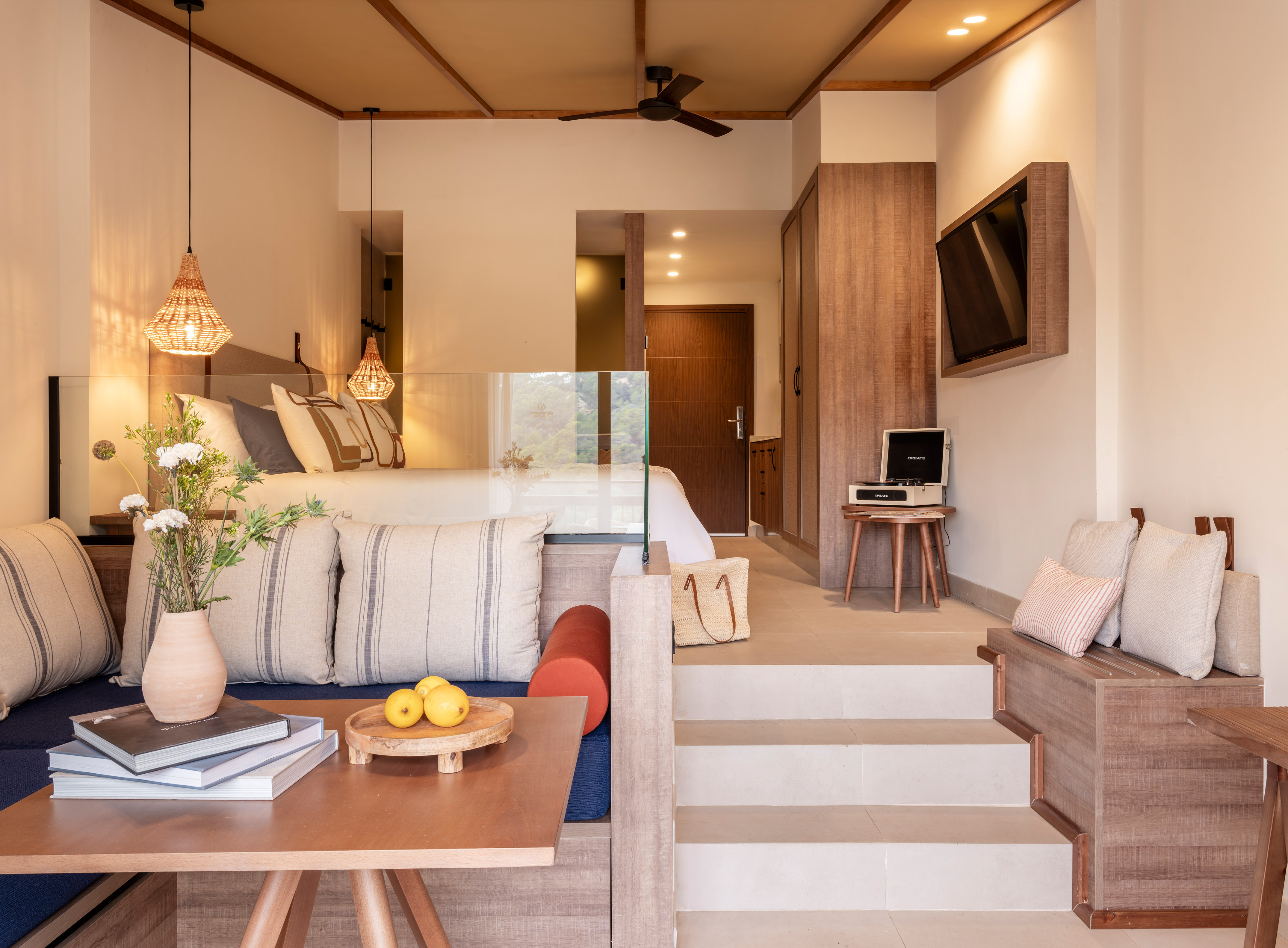 Modern resort suite with bed, lounge area, TV, and natural wood decor.