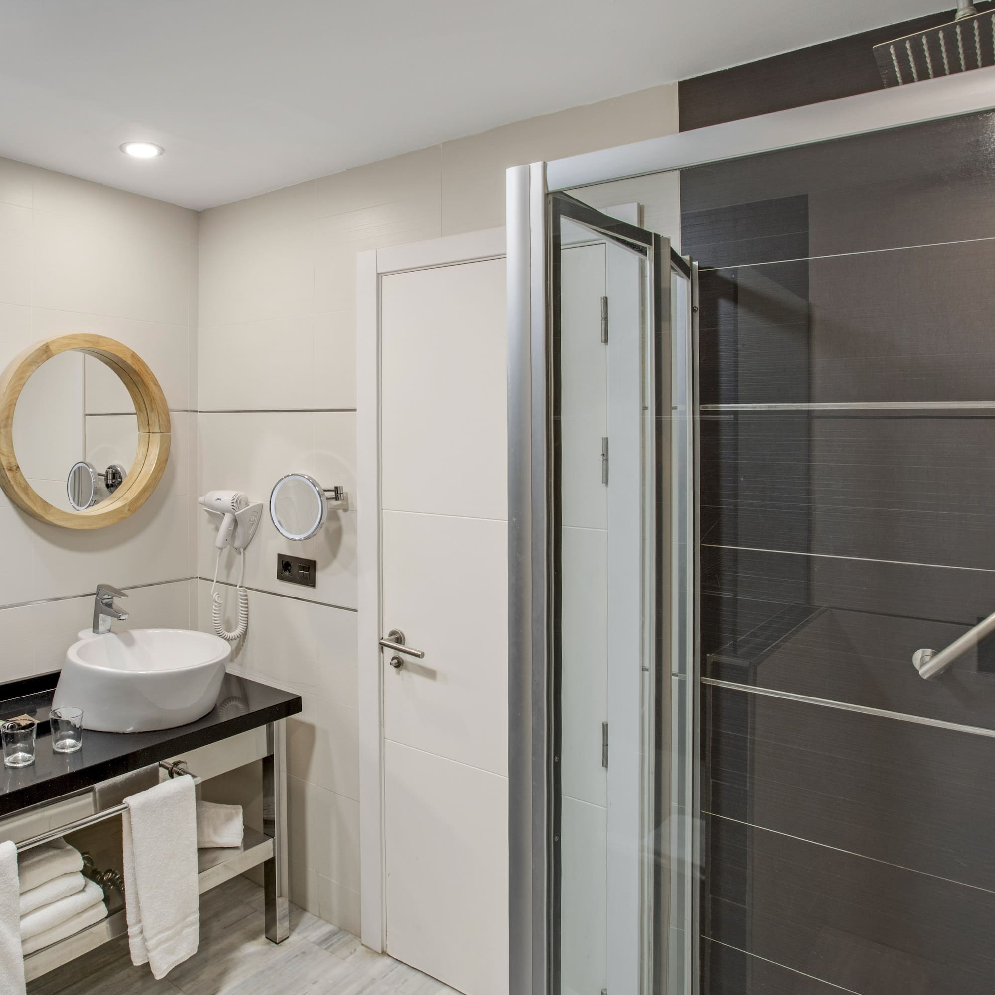 Hotel bathroom with double vanity, wooden mirrors, and dark tiled shower.