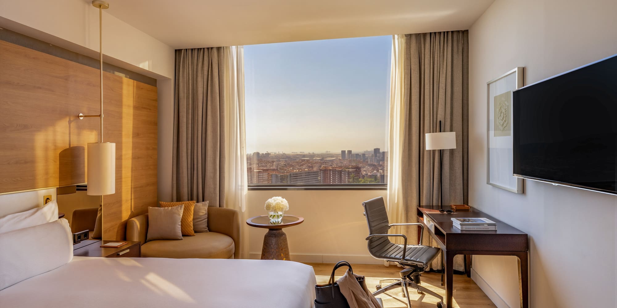 Modern hotel room with large bed, desk, city view, and lounge seating.
