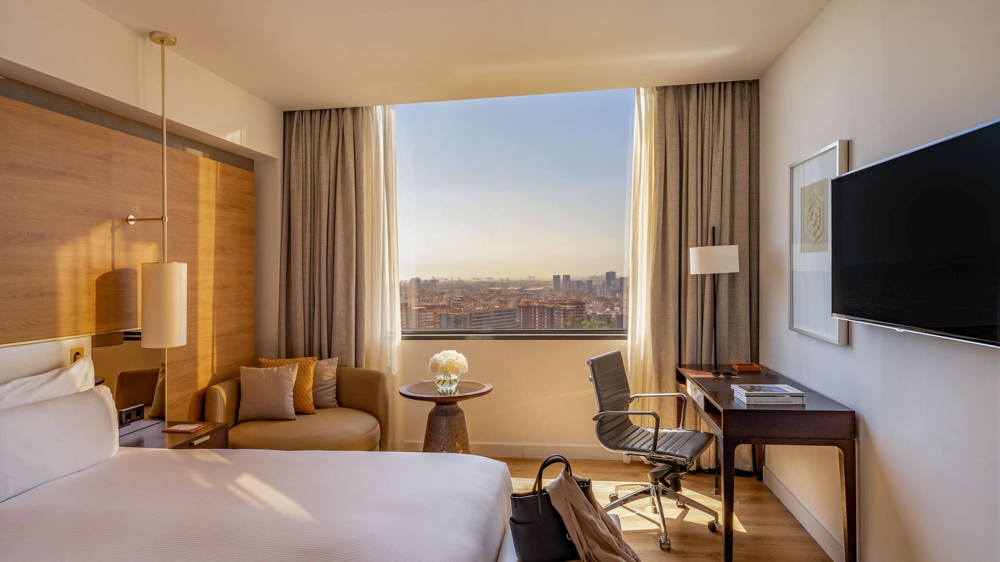 Modern hotel room with large bed, desk, city view, and lounge seating.