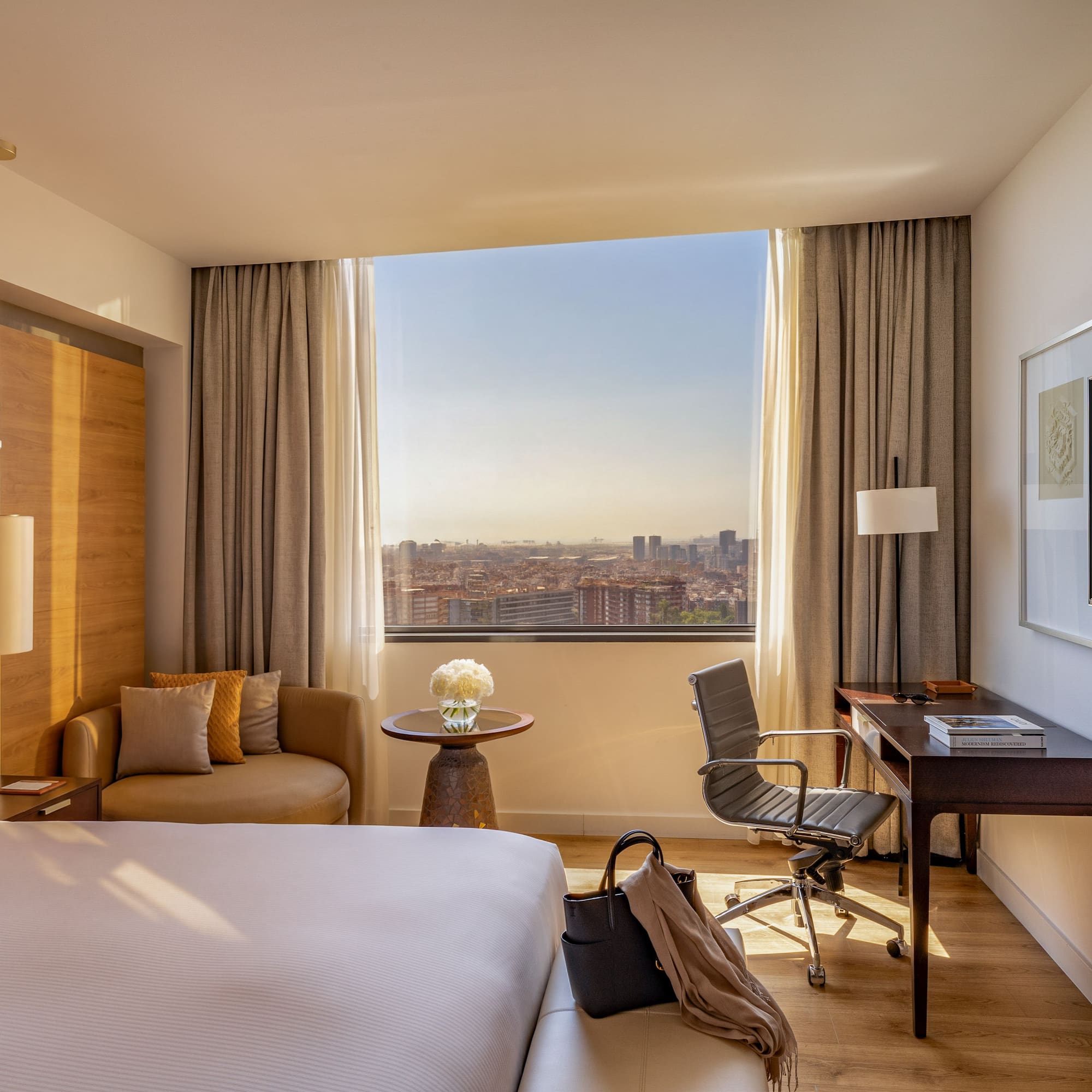 Modern hotel room with large bed, desk, city view, and lounge seating.