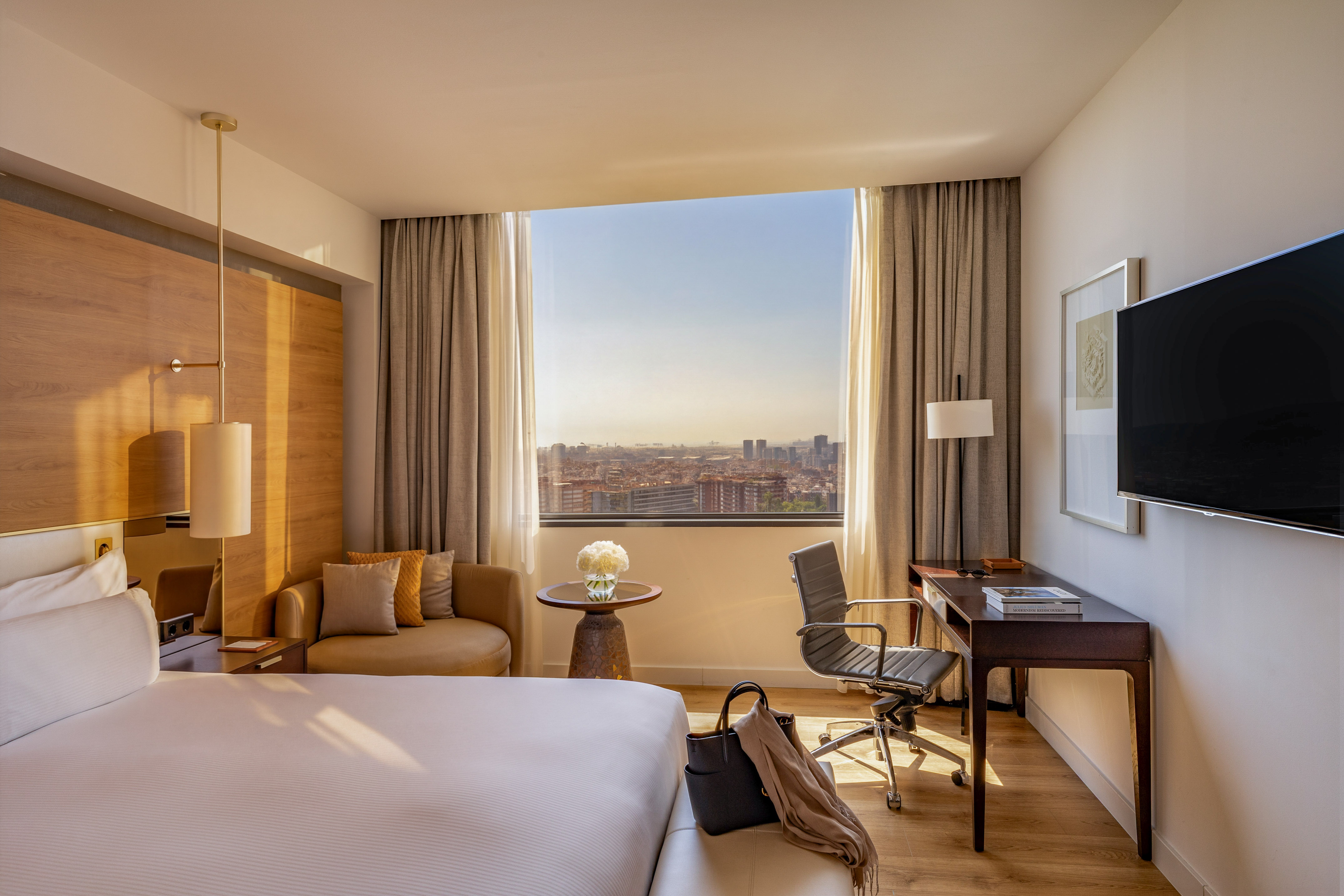 Modern hotel room with large bed, desk, city view, and lounge seating.