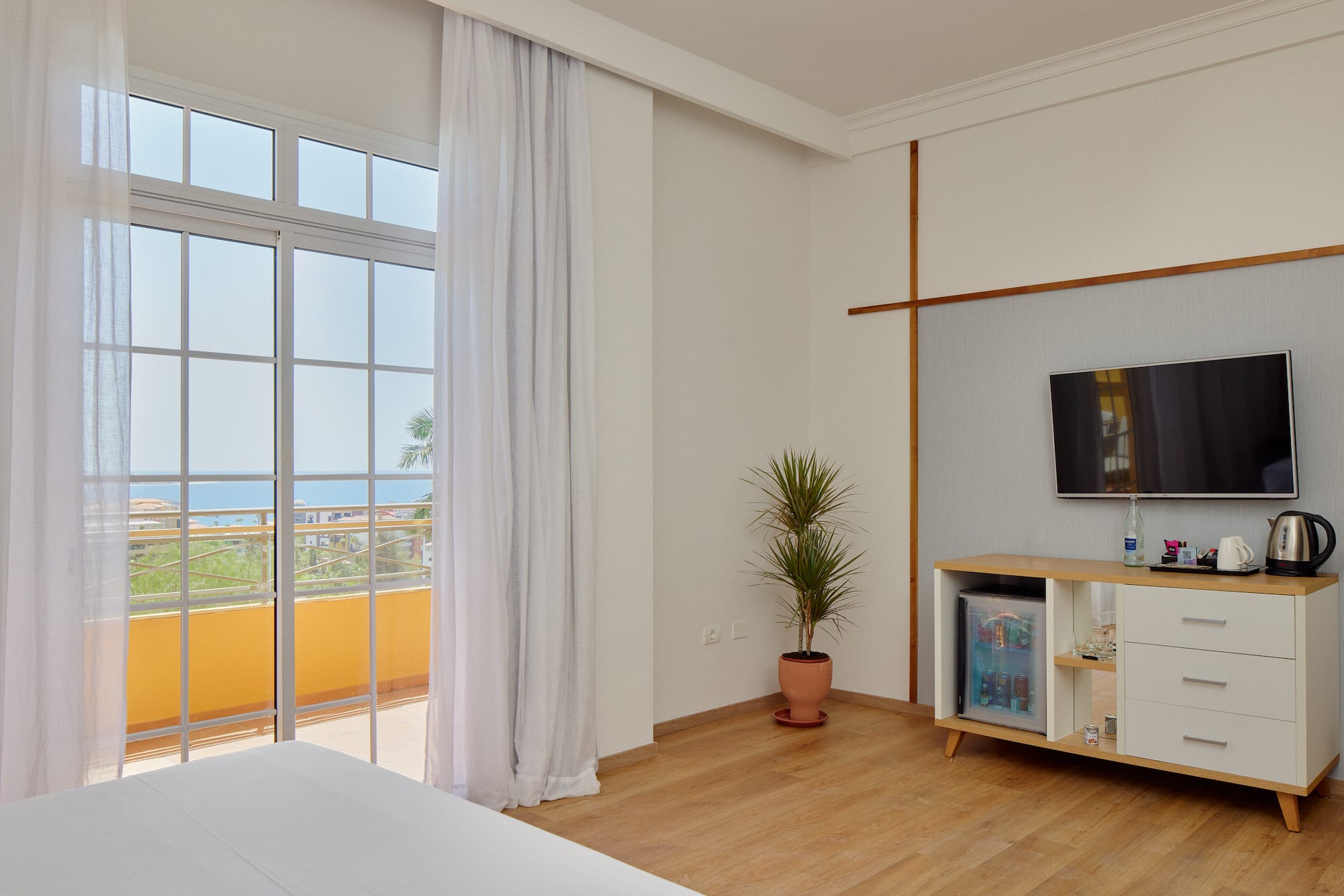 Modern hotel room with ocean view balcony, bed, TV, and minibar.