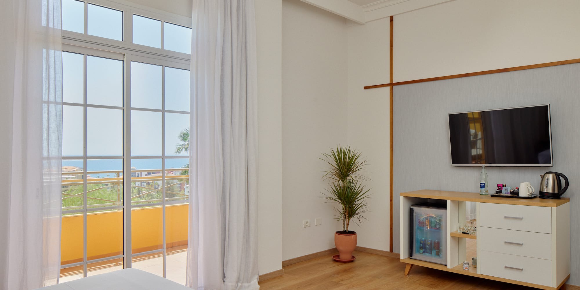 Modern hotel room with ocean view balcony, TV, and mini-fridge.