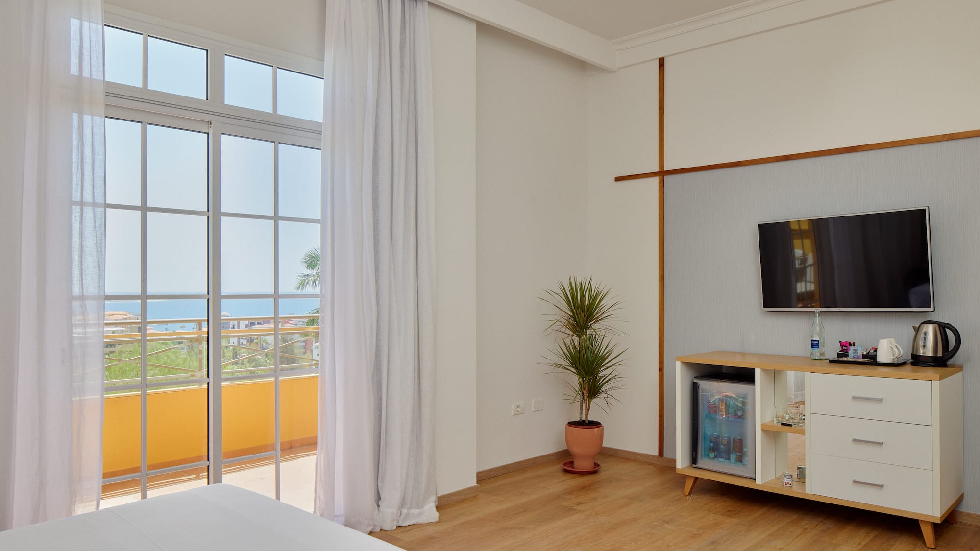 Modern hotel room with ocean view balcony, bed, TV, and minibar.