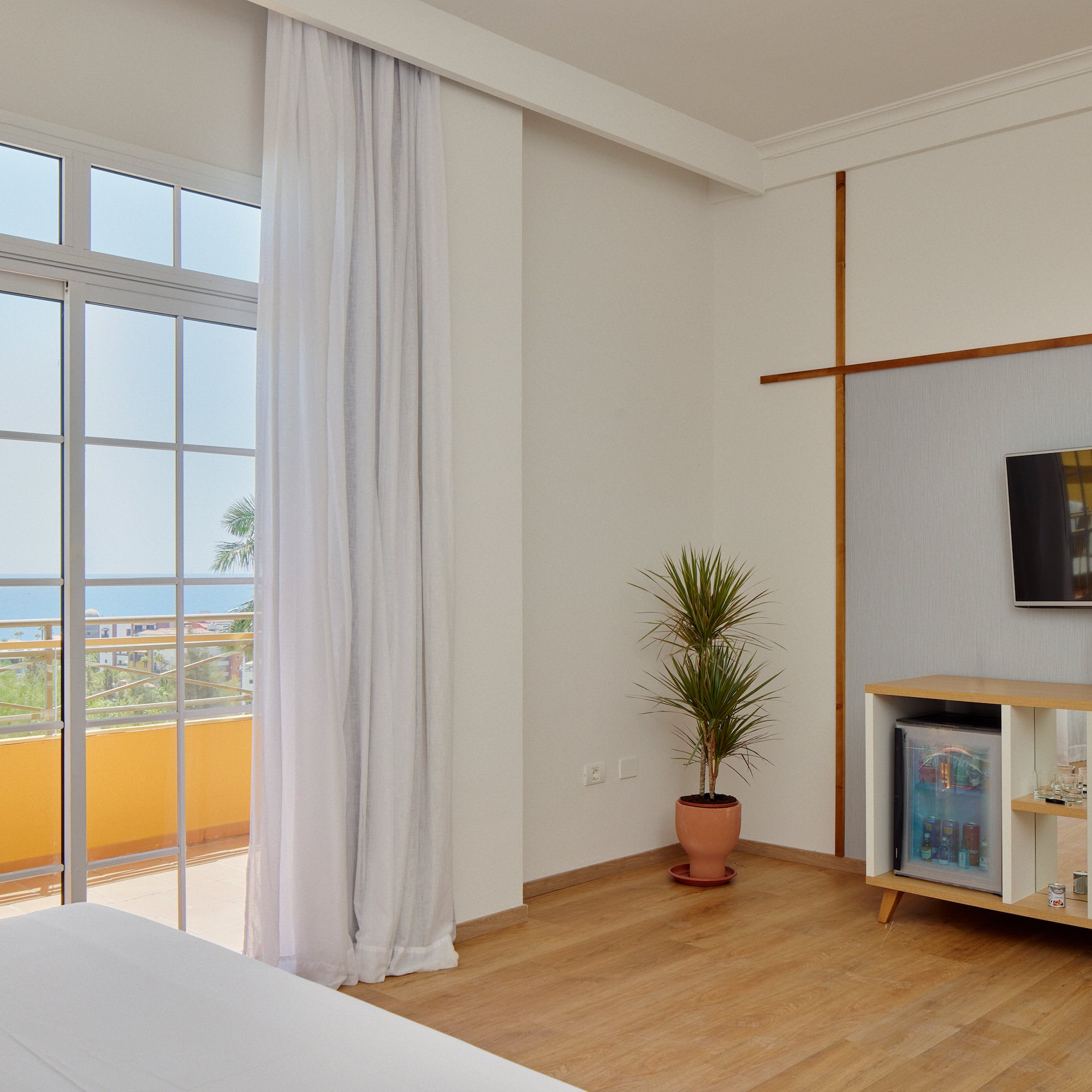 Modern hotel room with ocean view balcony, bed, TV, and minibar.