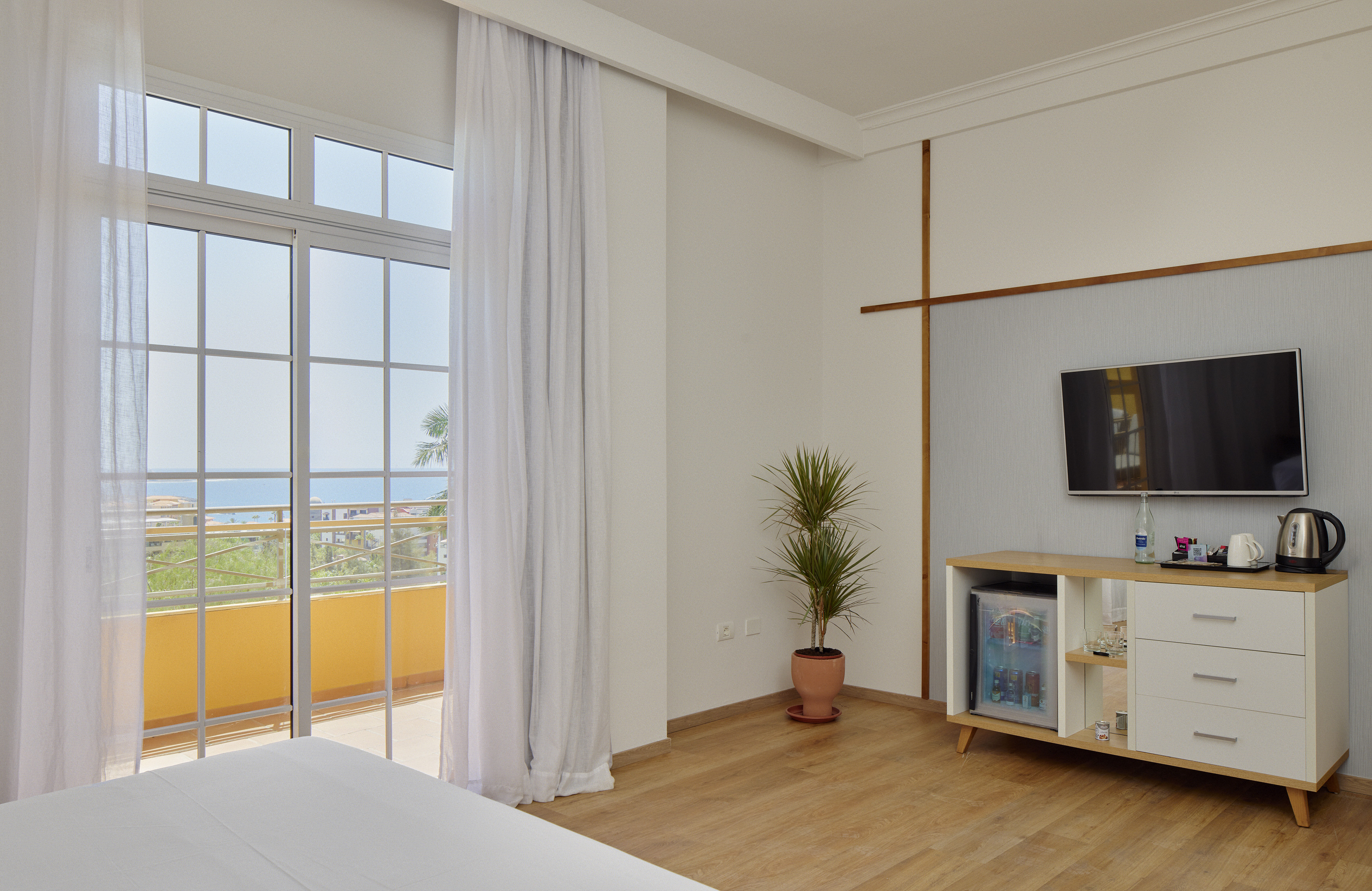 Modern hotel room with ocean view balcony, bed, TV, and minibar.