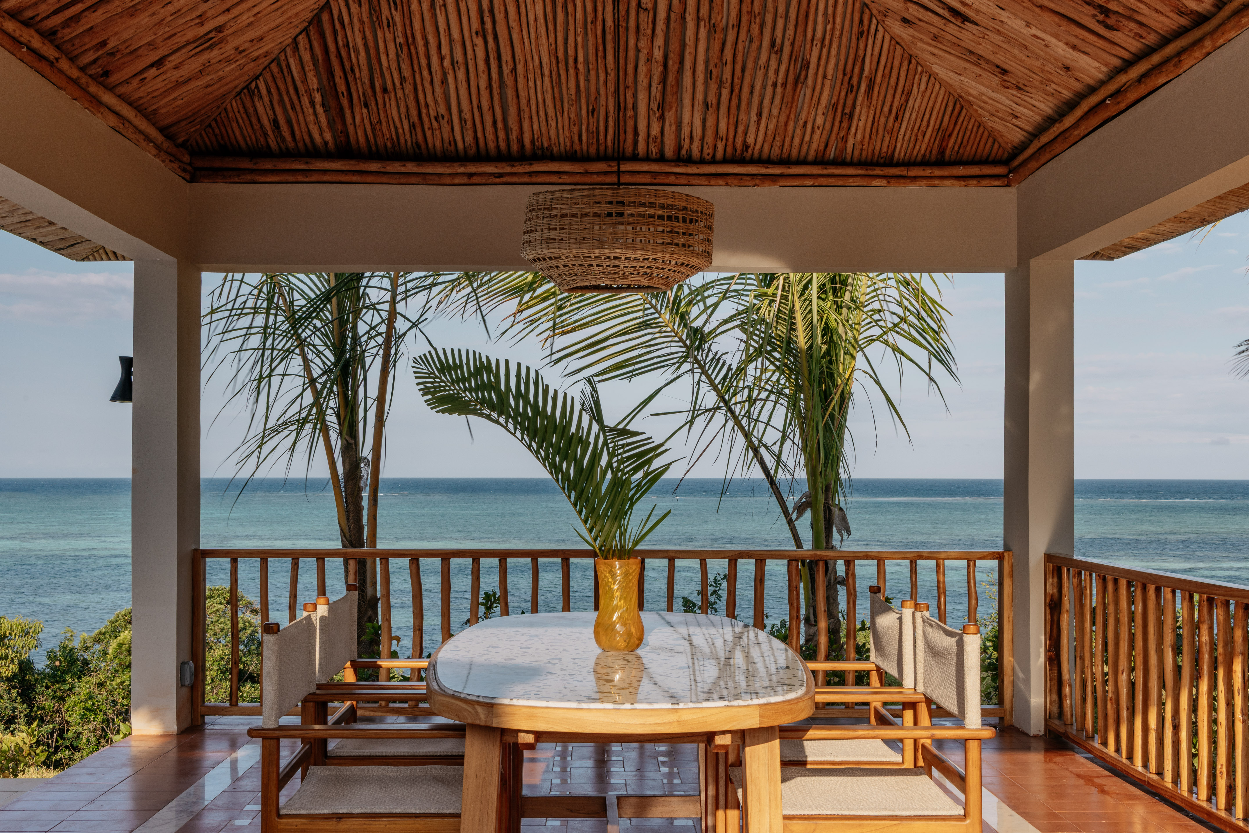 Tropical resort patio with ocean view, wooden table, and palm trees.