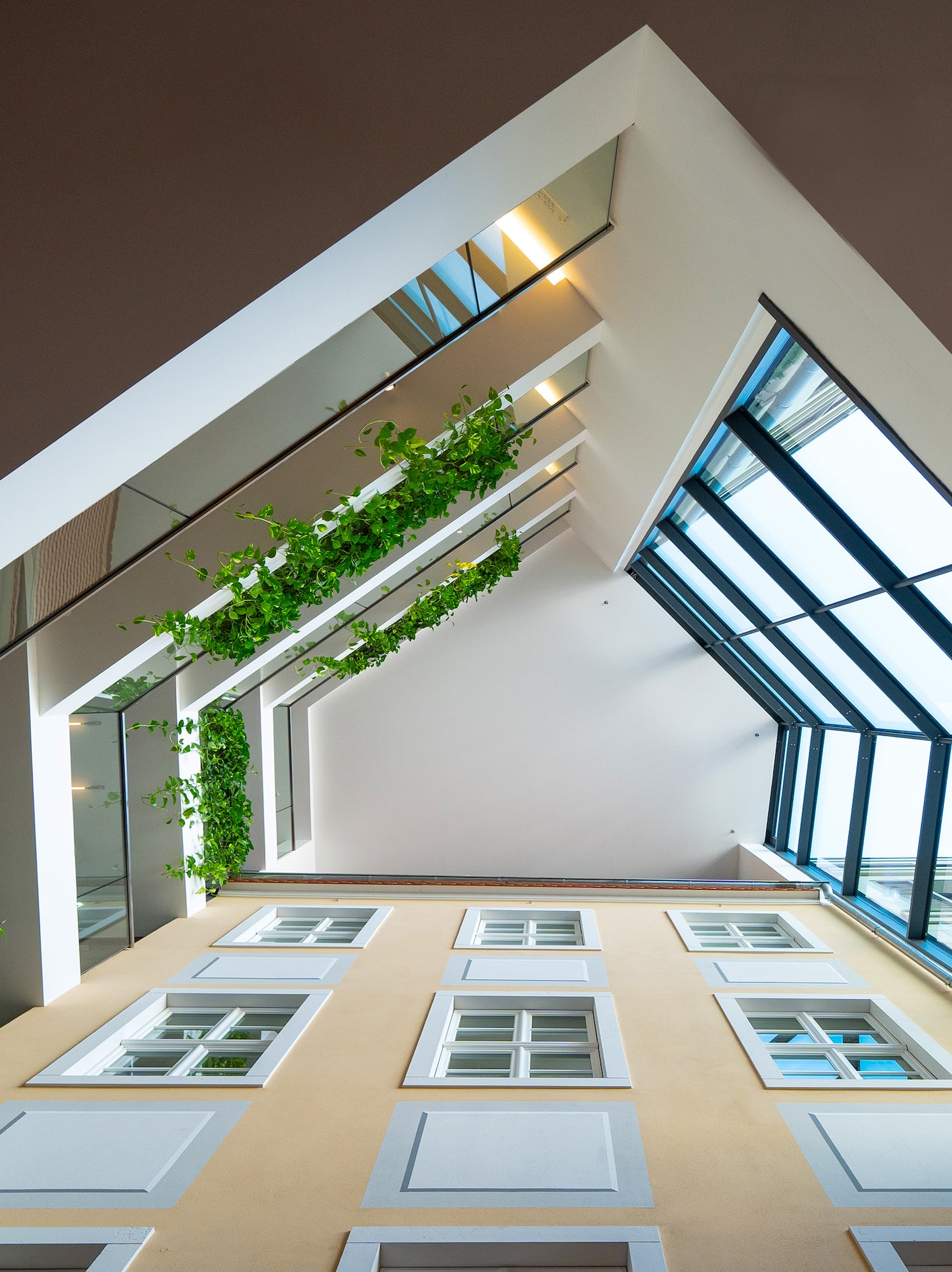Modern atrium with yellow facade, green vines, and angular glass skylights.