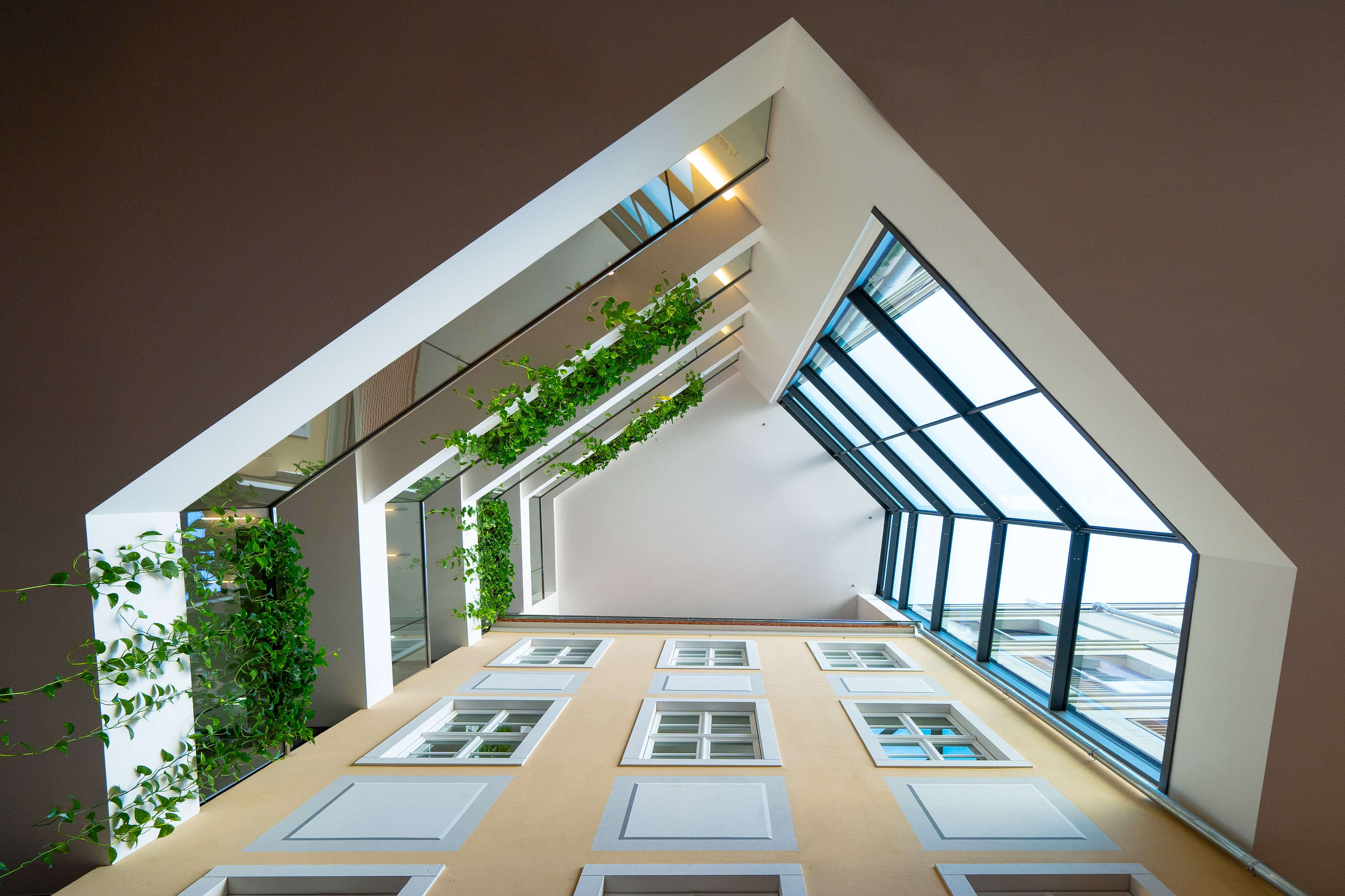 Modern atrium with yellow facade, green vines, and angular glass skylights.