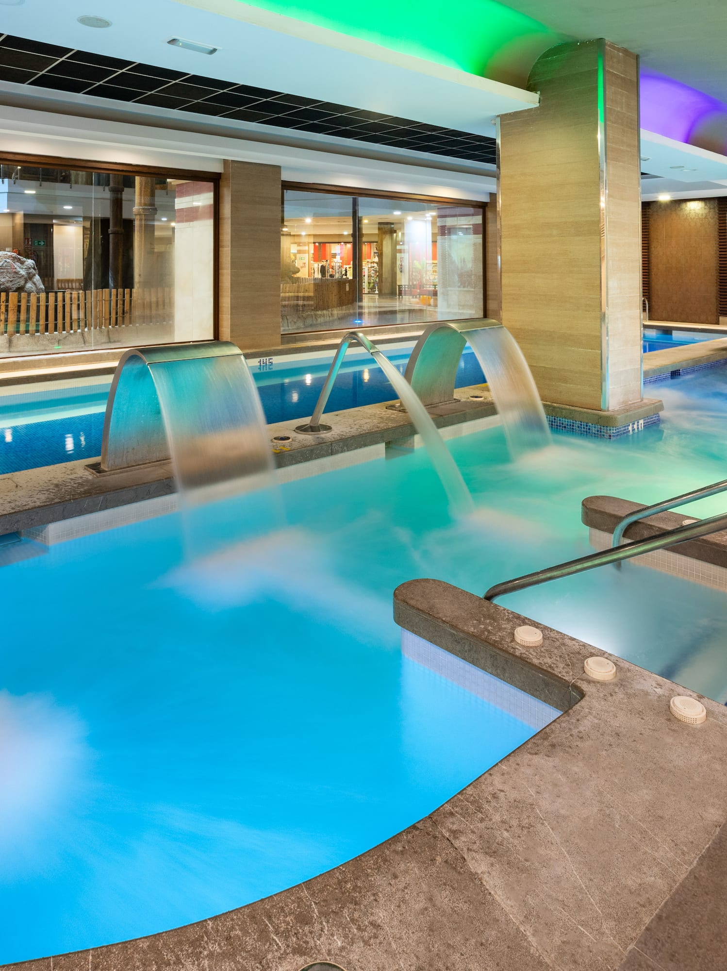 Luxury indoor spa pool with hydrotherapy jets, waterfalls, and colorful lighting.