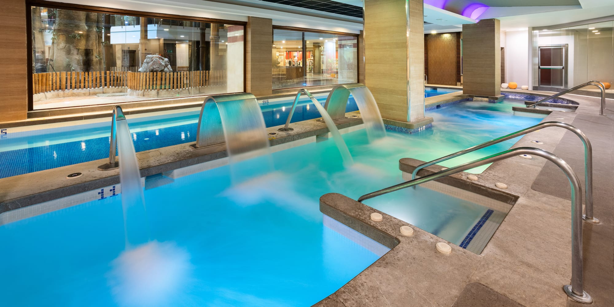 Indoor spa pool with hydrotherapy jets, colorful lighting, and large windows.