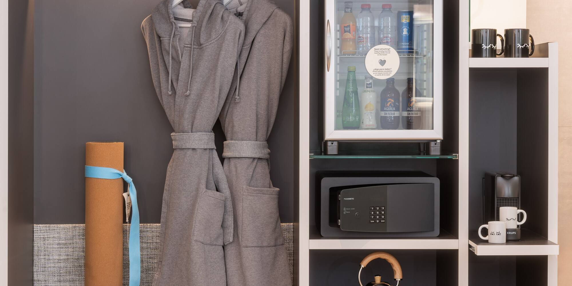 Hotel wardrobe with bathrobes, mini-bar, safe, yoga mat, and coffee setup.