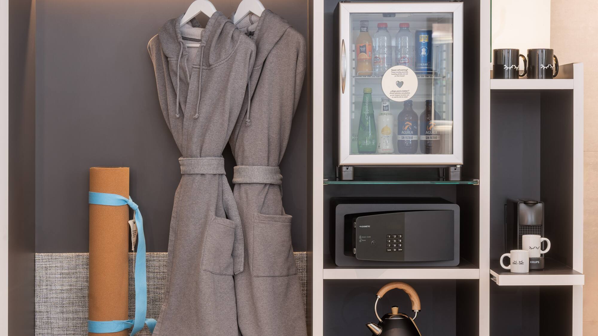 Hotel wardrobe with bathrobes, mini-bar, safe, yoga mat, and coffee setup.