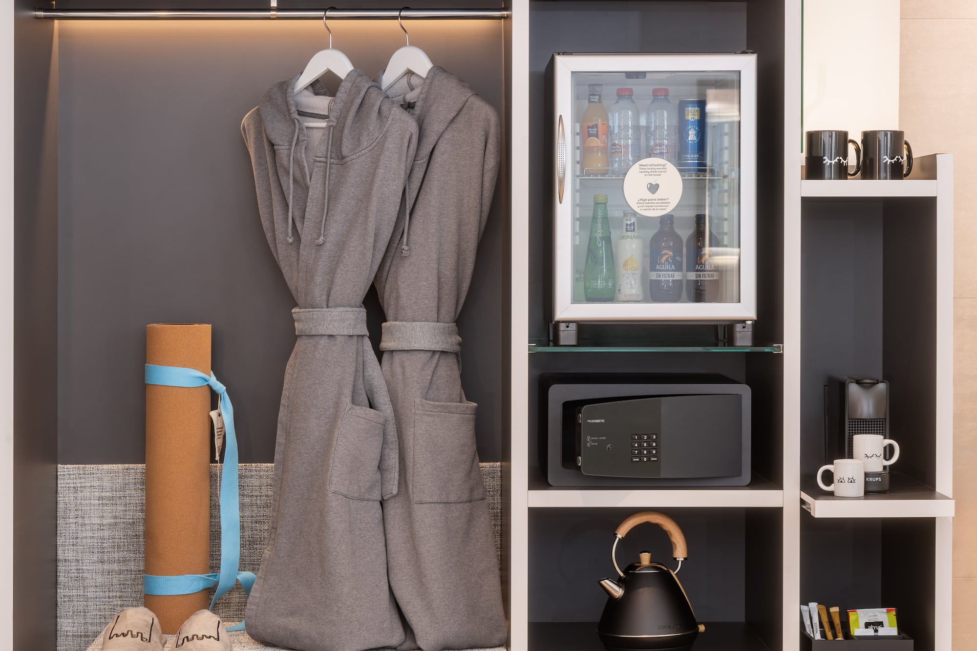 Hotel wardrobe with bathrobes, mini-bar, safe, yoga mat, and coffee setup.