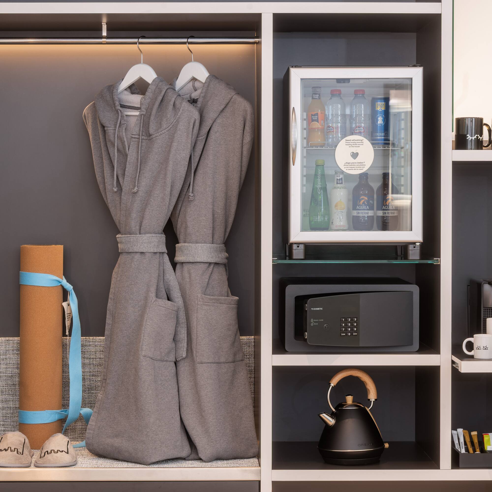 Hotel wardrobe with bathrobes, mini-bar, safe, yoga mat, and coffee setup.
