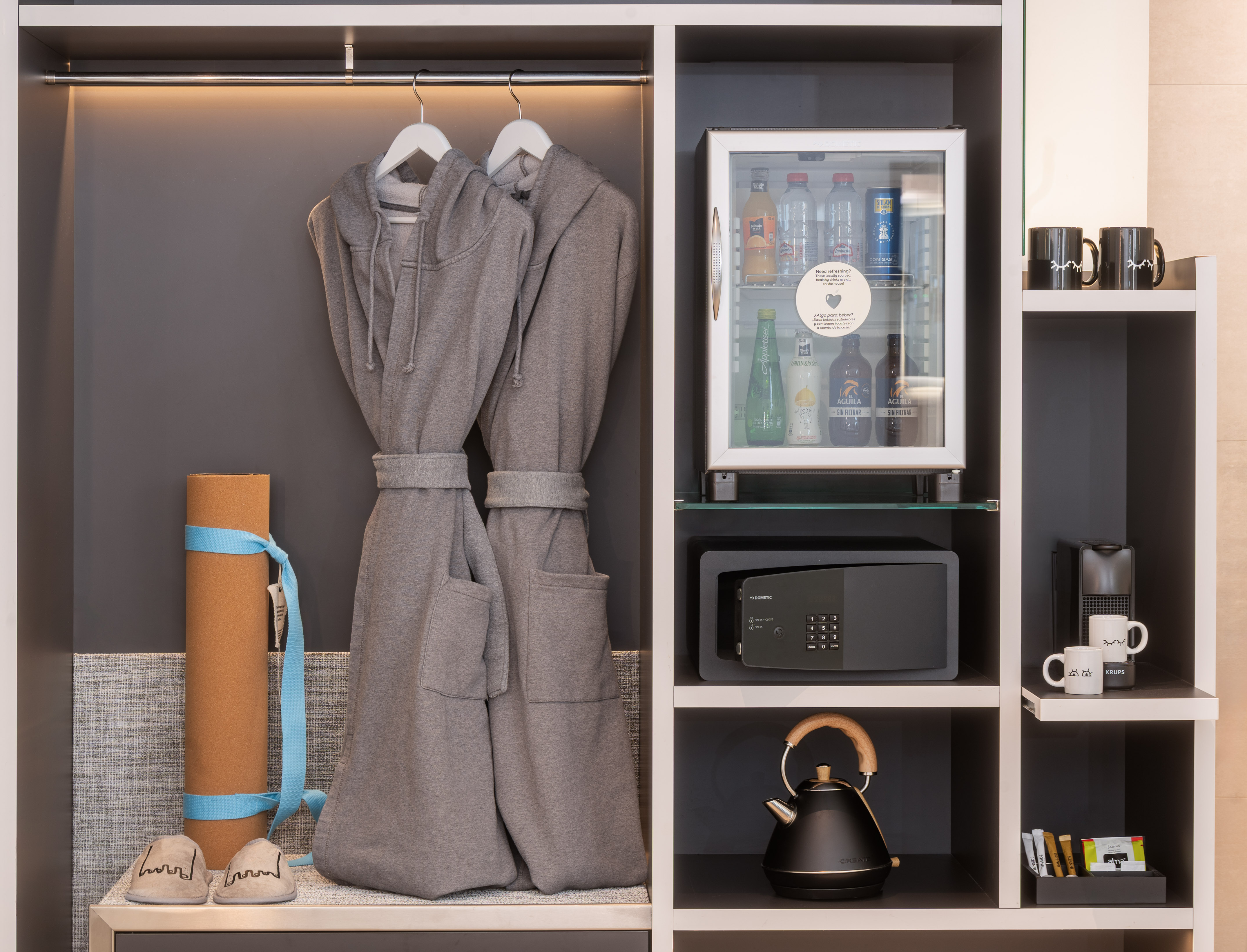 Hotel wardrobe with bathrobes, mini-bar, safe, yoga mat, and coffee setup.