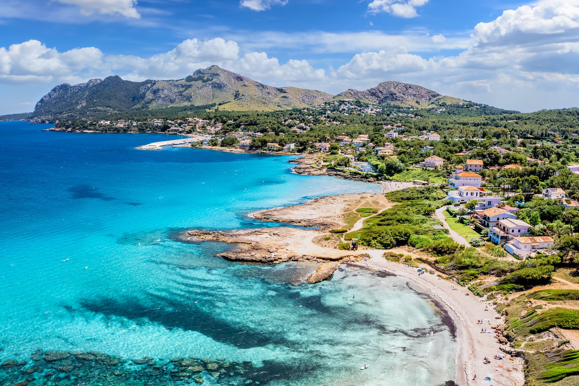 Turquoise Mediterranean coast, sandy beach, coastal village, and green mountains.