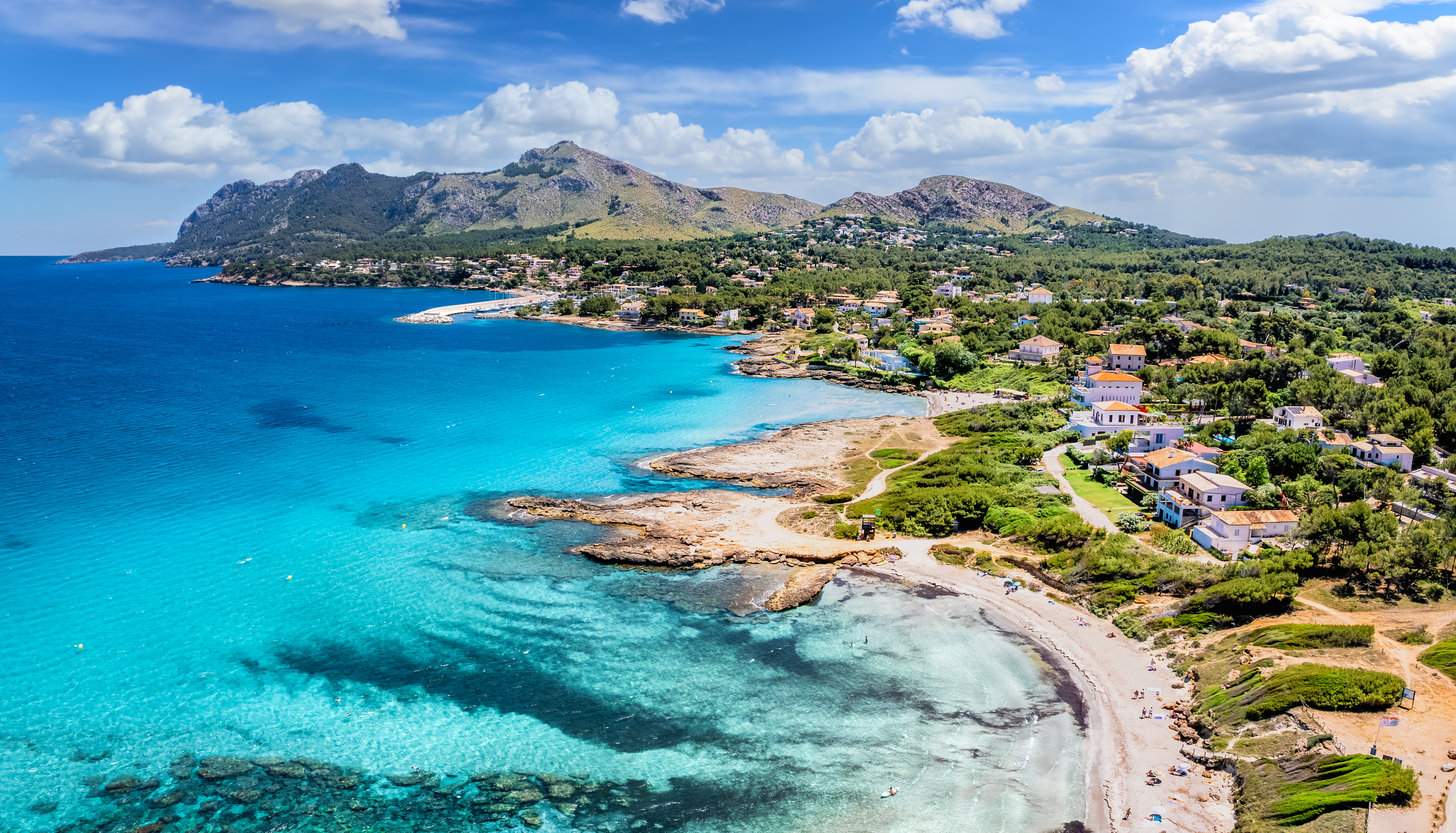 Cala de aguas turquesas en Mallorca, con playa, casas costeras y montañas.