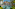 Tropical resort pool with palm trees, blue umbrellas, and hotel buildings.