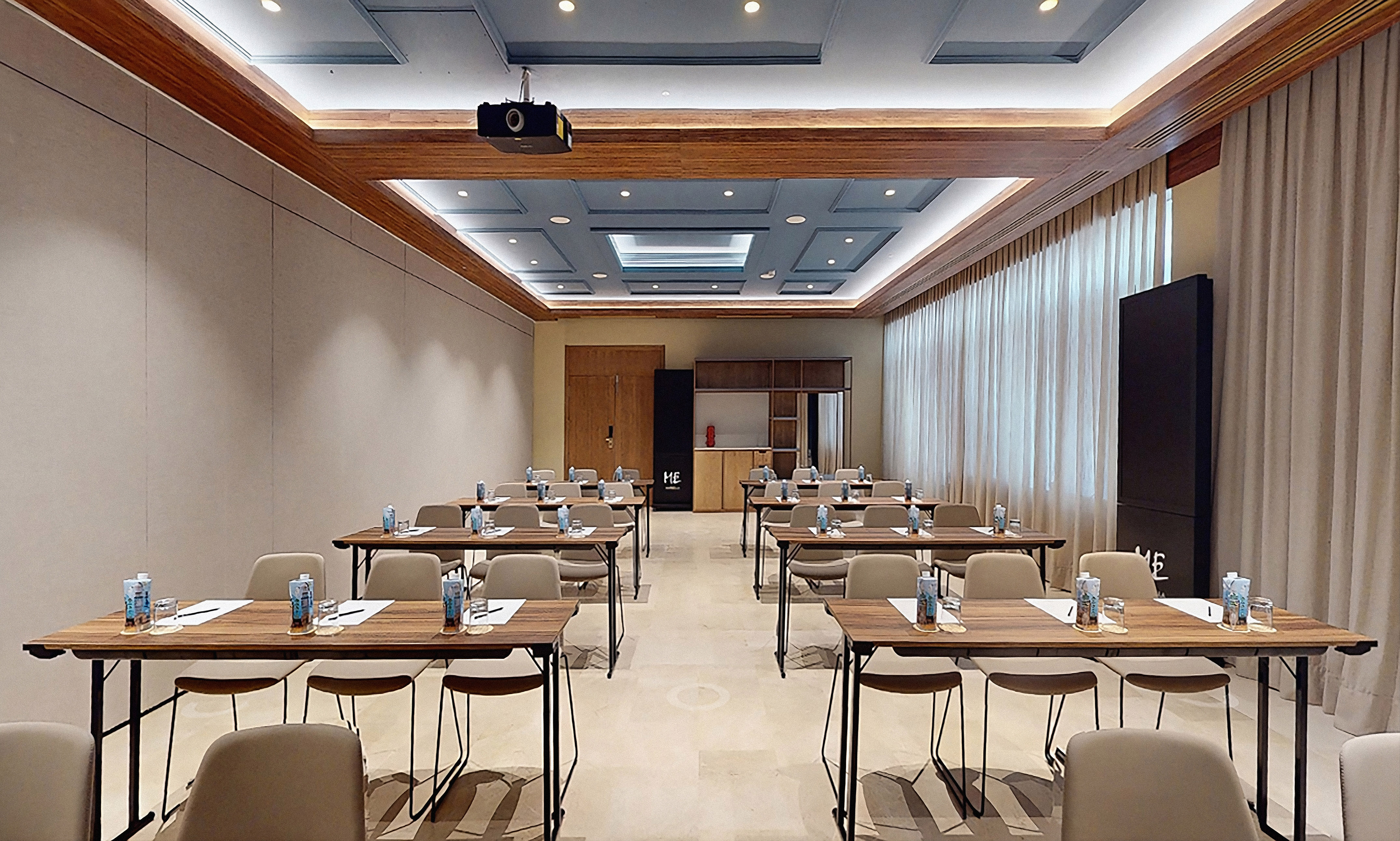 Modern conference room with rows of tables, chairs, ceiling projector, and screen.