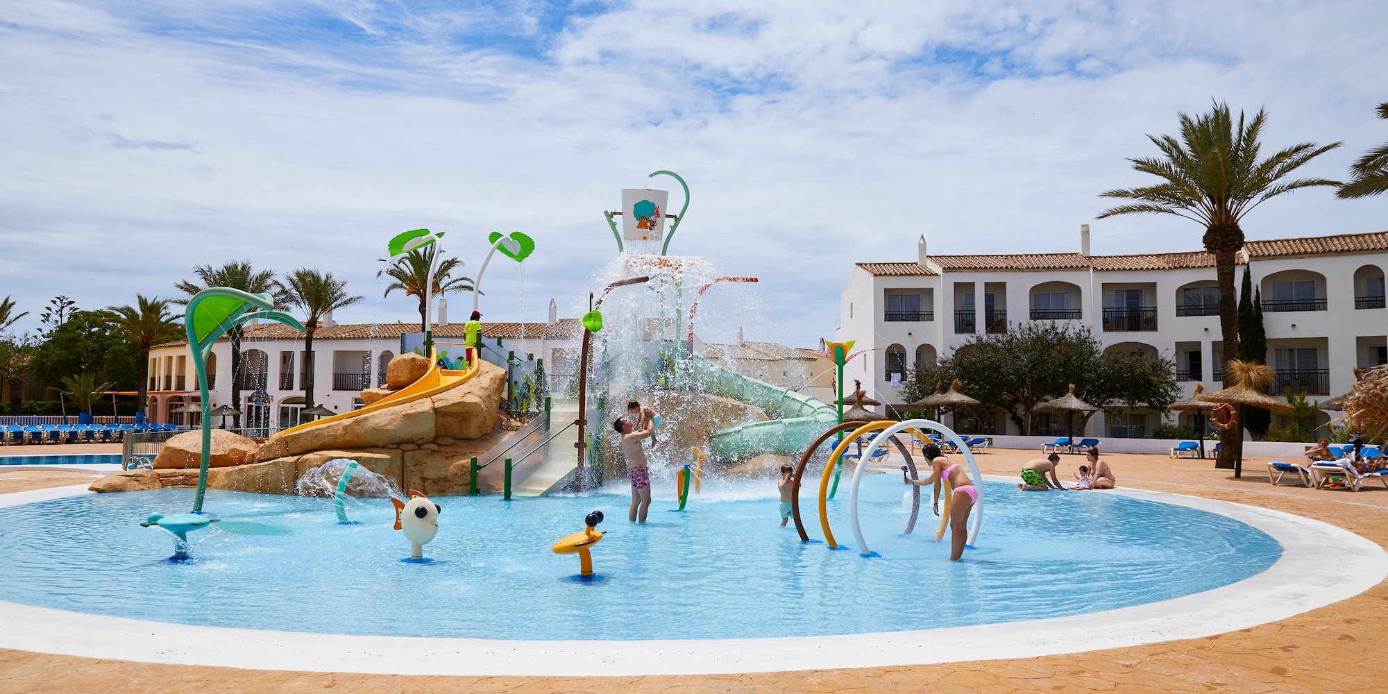 Kids splash park at resort with slides, water features, and children playing.