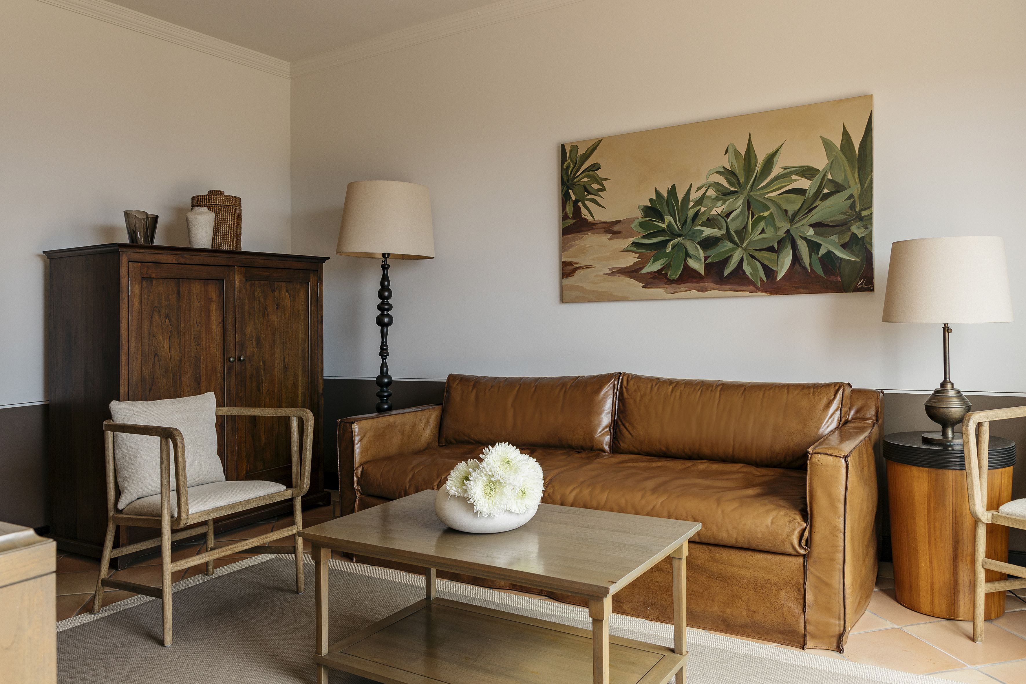 Cozy living room with brown leather sofa, wooden furniture, and plant artwork.