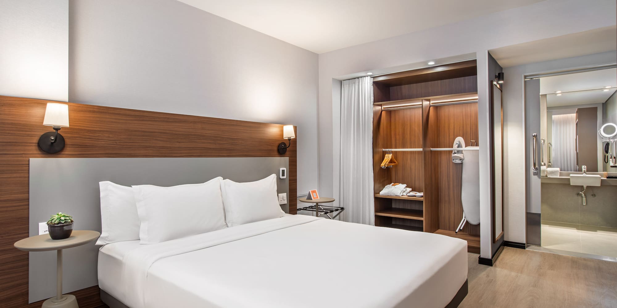 Spacious modern hotel room with king bed, wardrobe, and bathroom view.