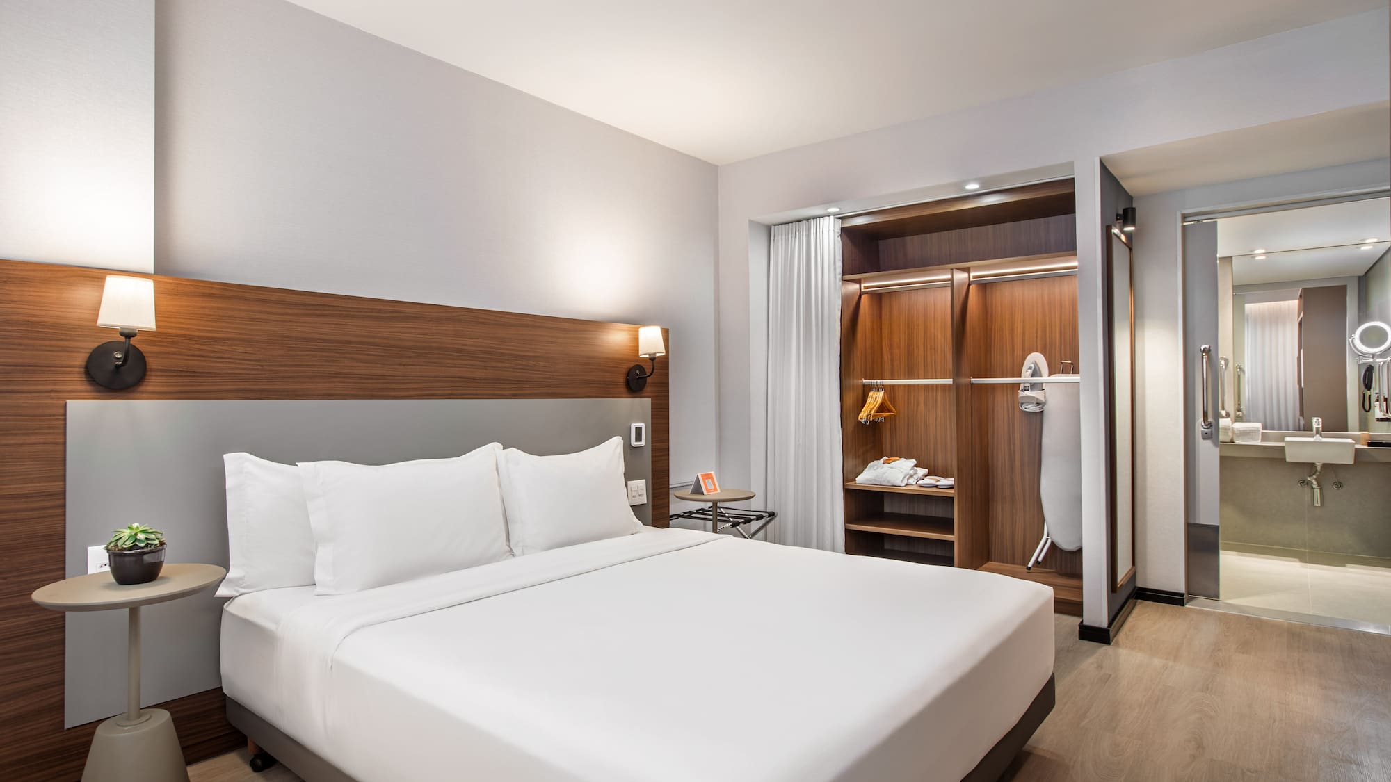 Spacious modern hotel room with king bed, wardrobe, and bathroom view.