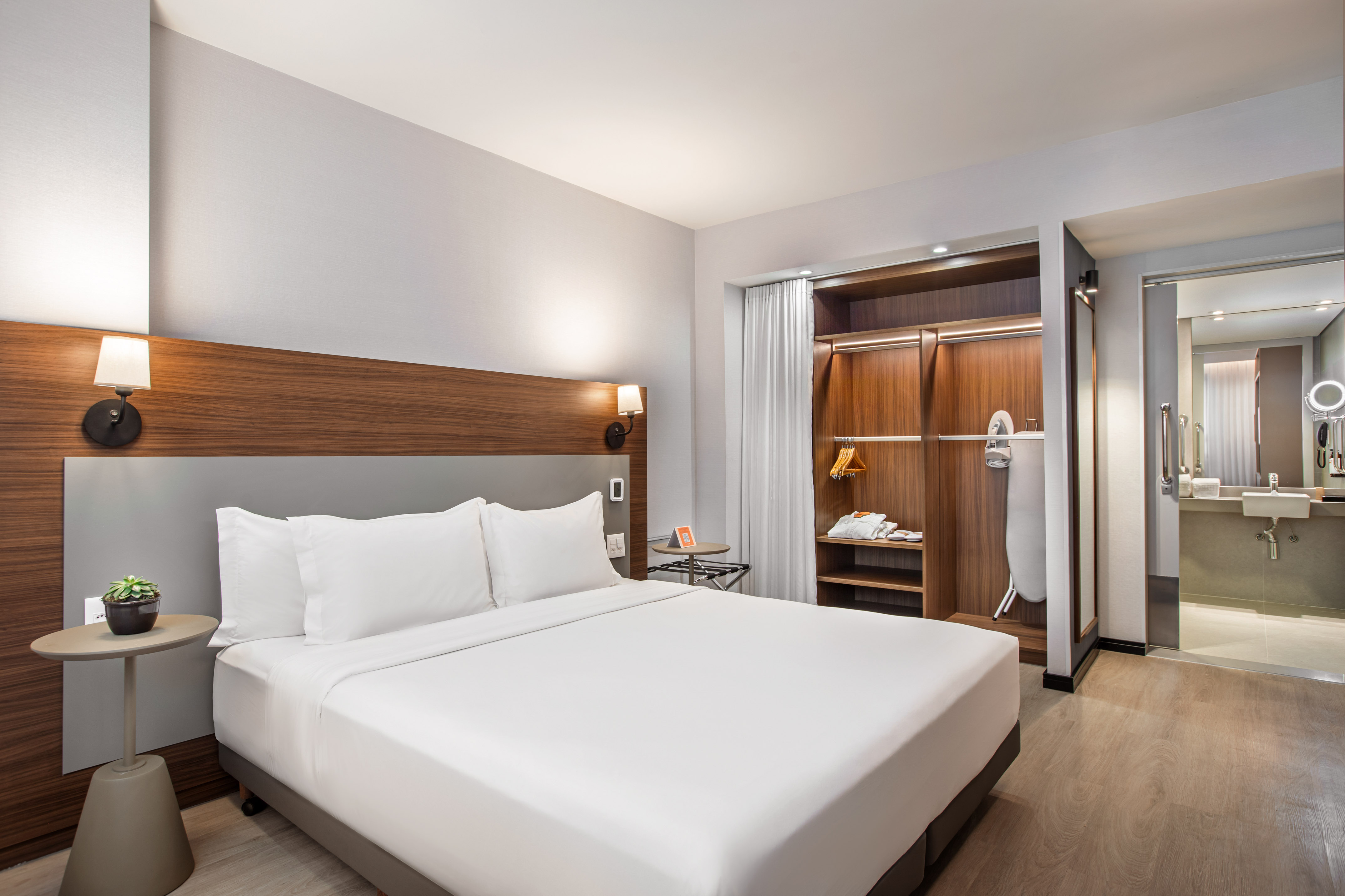 Spacious modern hotel room with king bed, wardrobe, and bathroom view.