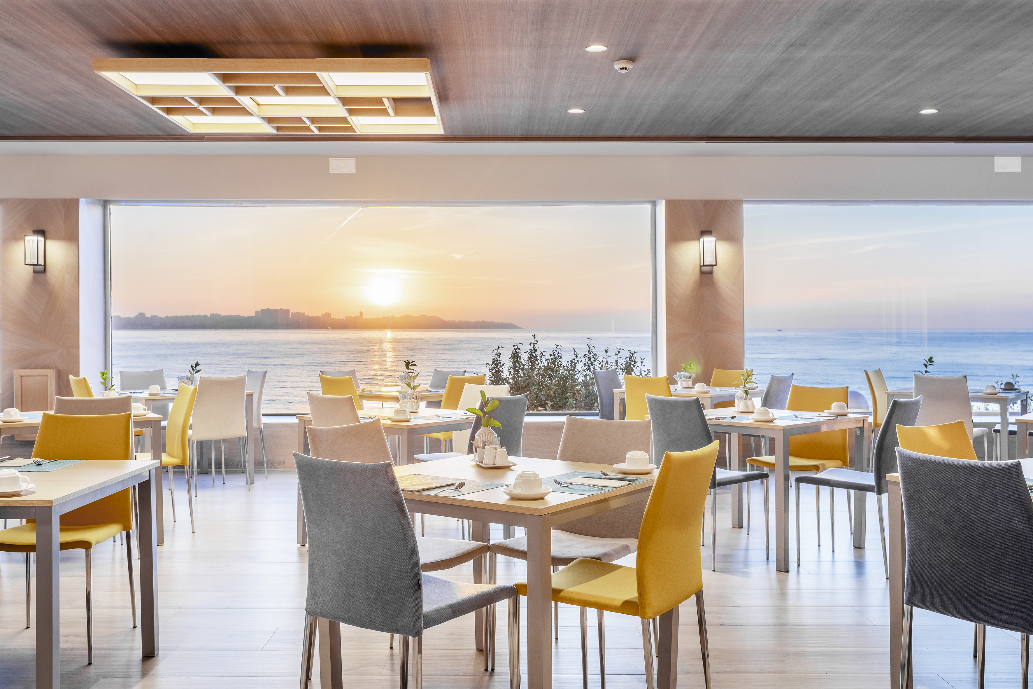 Restaurante hotel con vista panorámica al mar y mesas preparadas al atardecer.