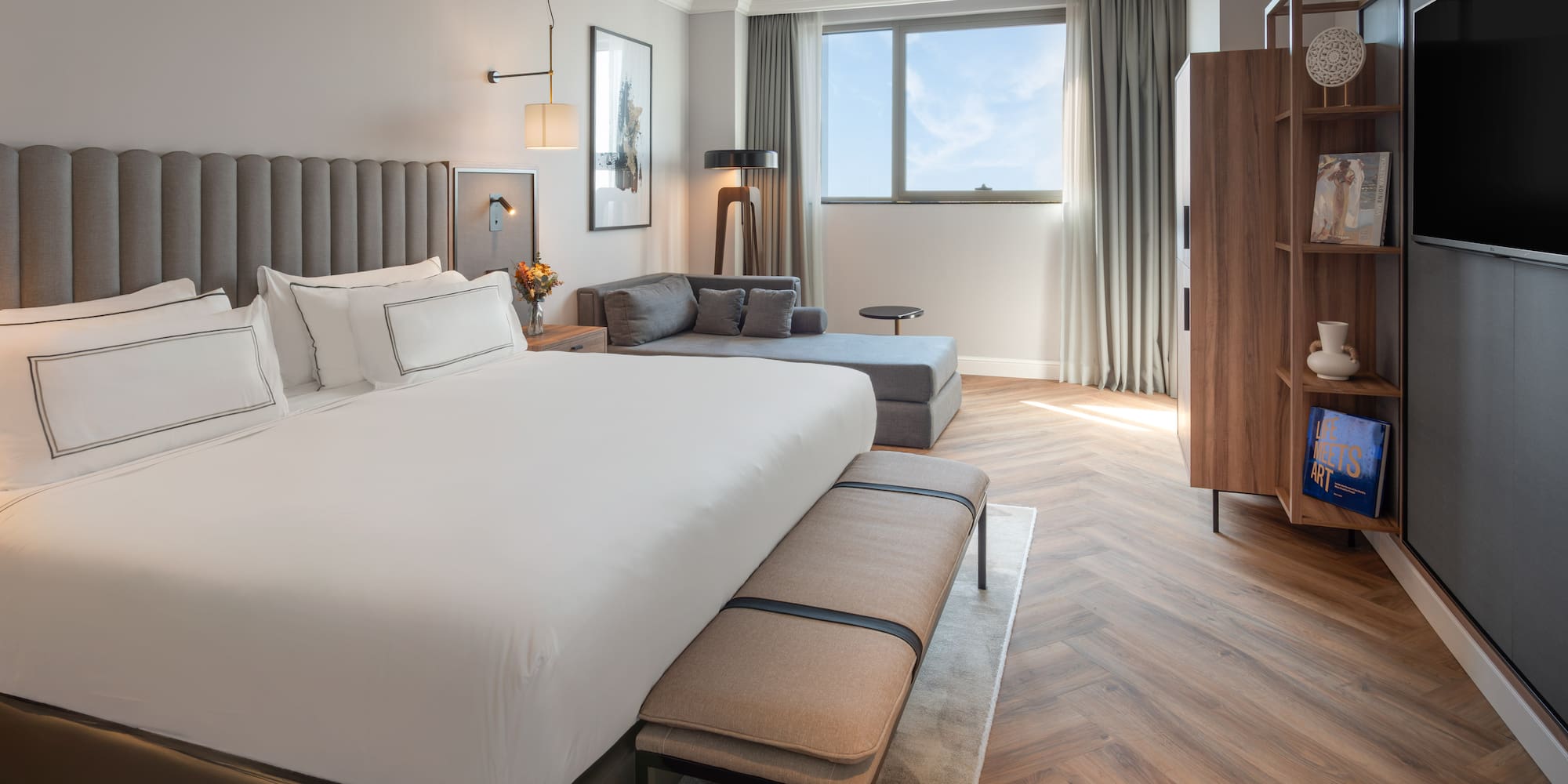 Lujosa habitación de hotel con cama king-size, chaise lounge y amplio ventanal.
