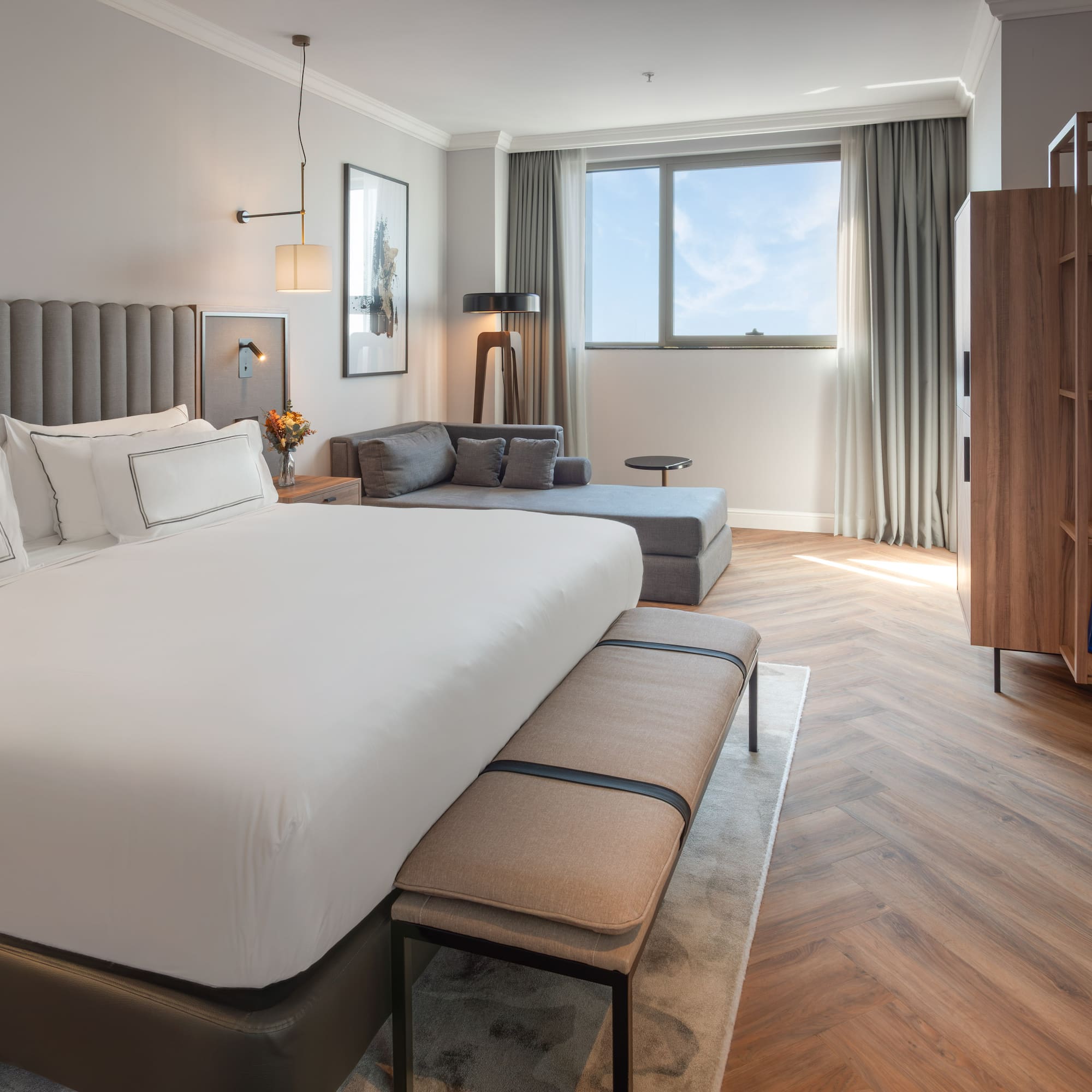 Suite de hotel moderna con cama king, chaise lounge, ventana y suelo de madera.