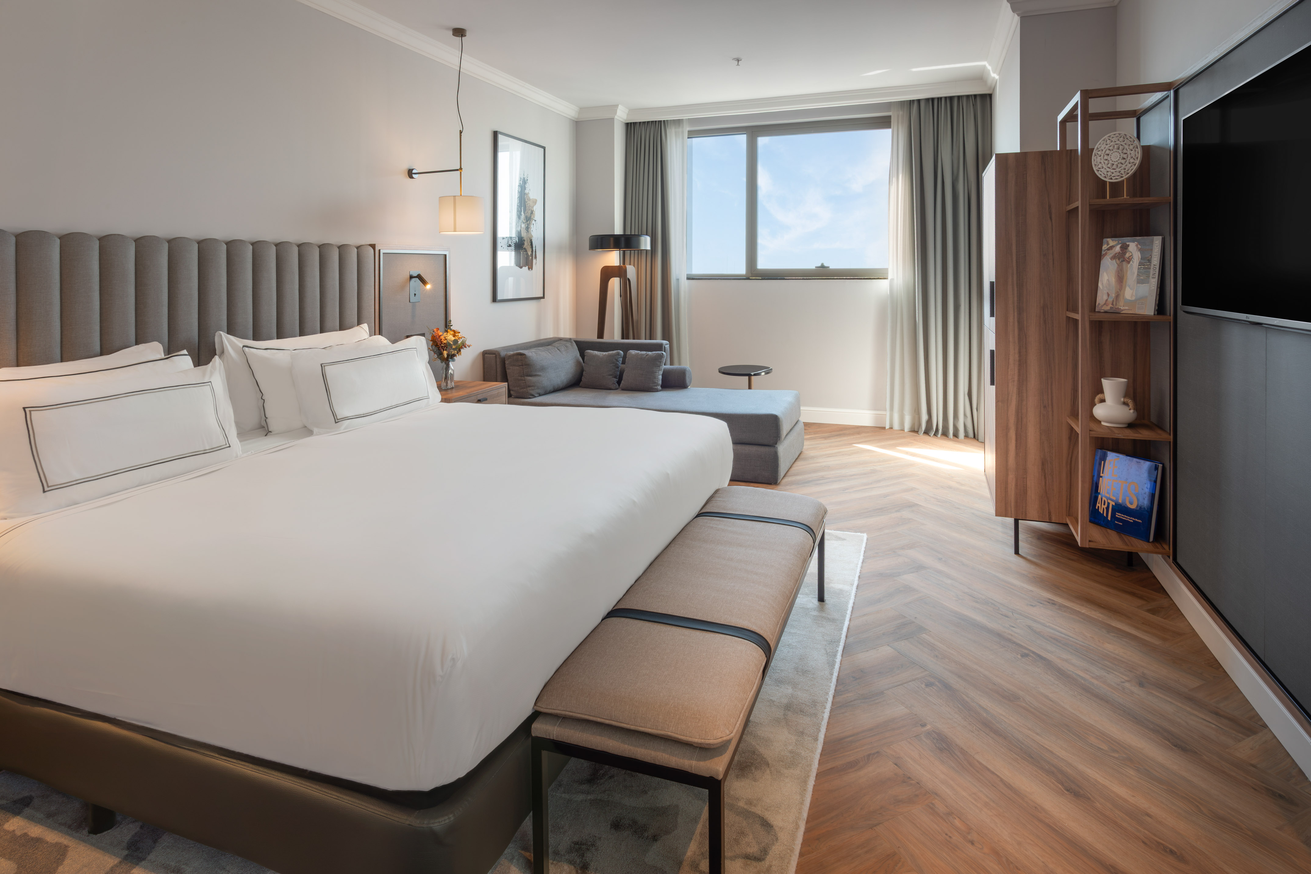 Suite de hotel moderna con cama king, chaise lounge, ventana y suelo de madera.